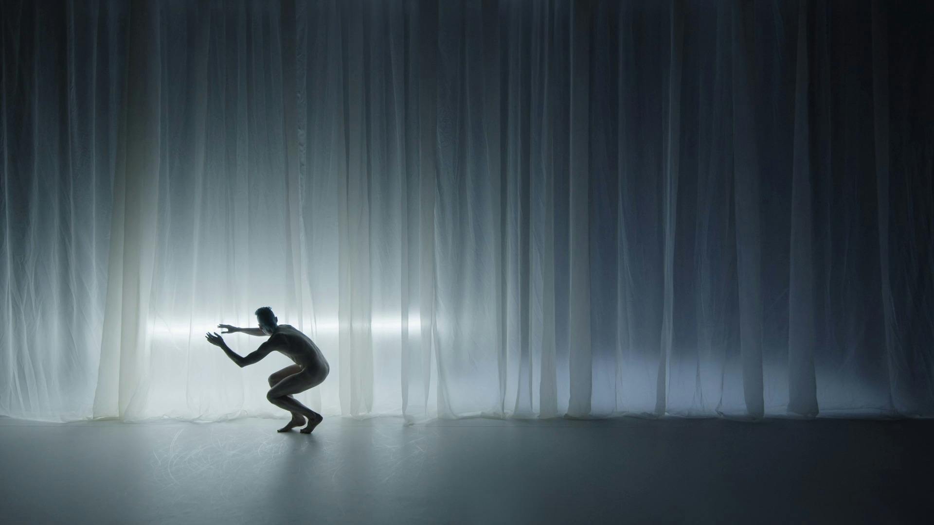 Un ballerino si abbassa e balla davanti a un grande sipario bianco