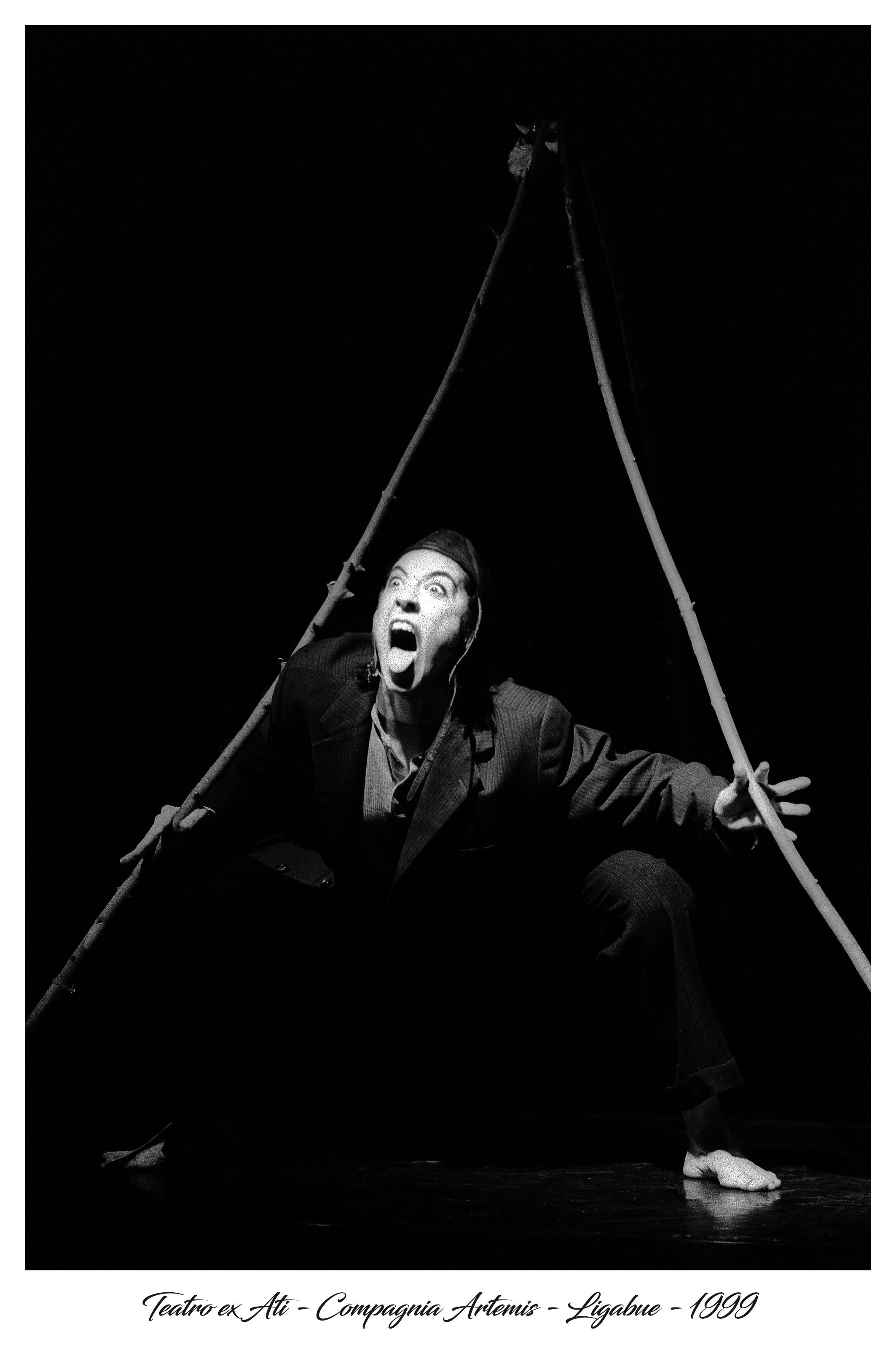 An artist shouts with his tongue hanging out of his mouth. He holds two long sticks.
