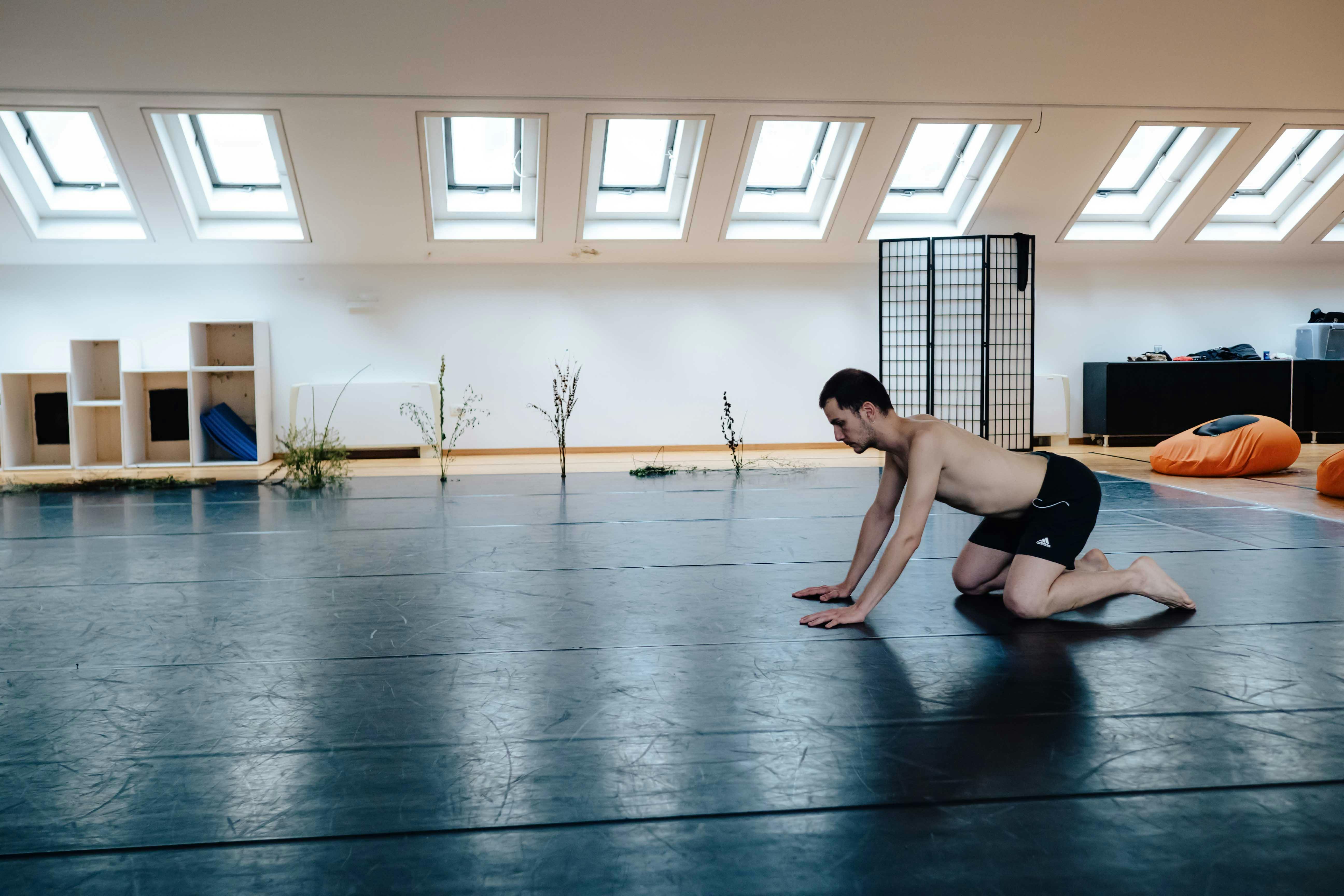 Fotografia di un performer inginocchiato in sala con composizioni floreali sullo sfondo
