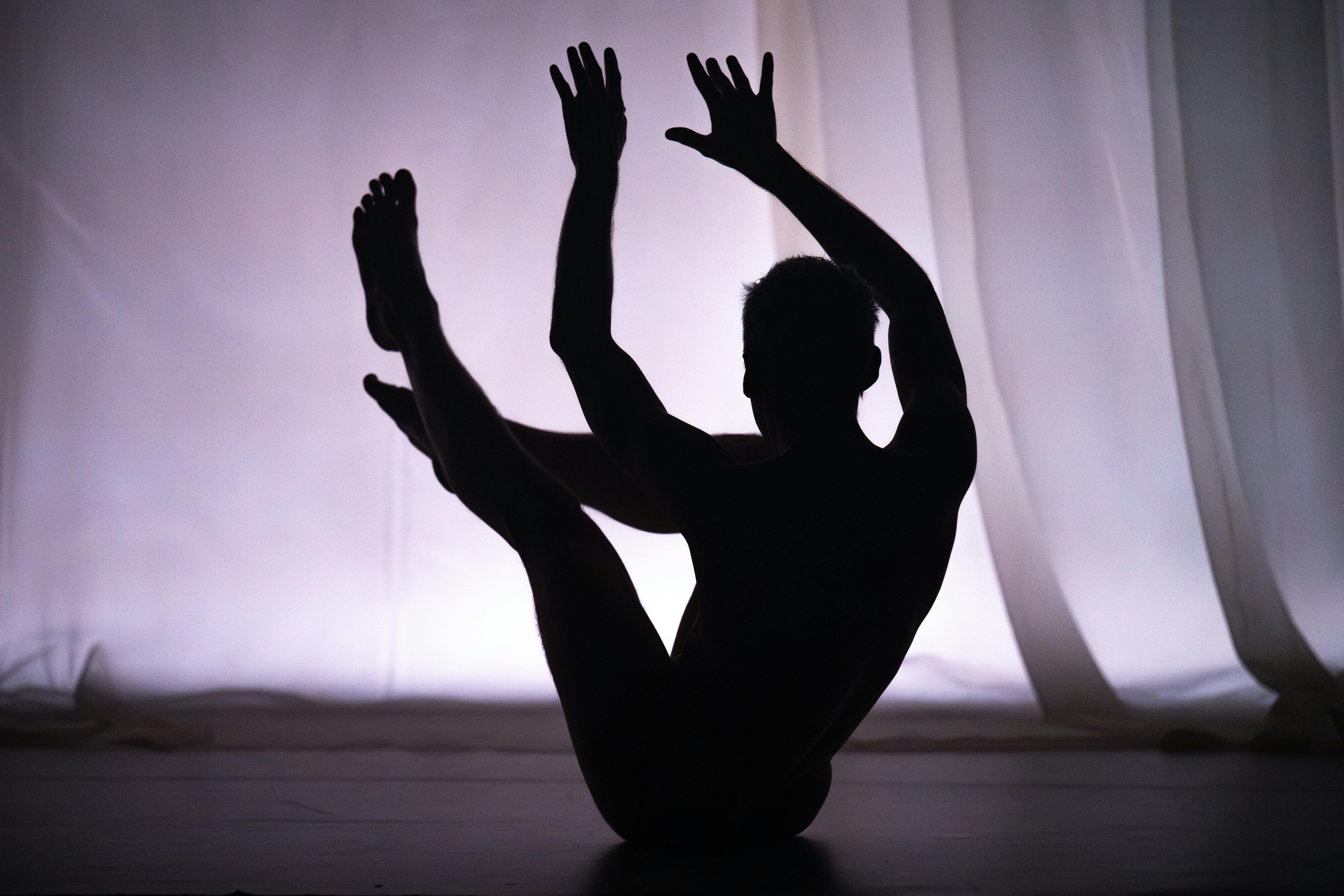 Un ballerino seduto in equilibrio con gambe e mani alzate