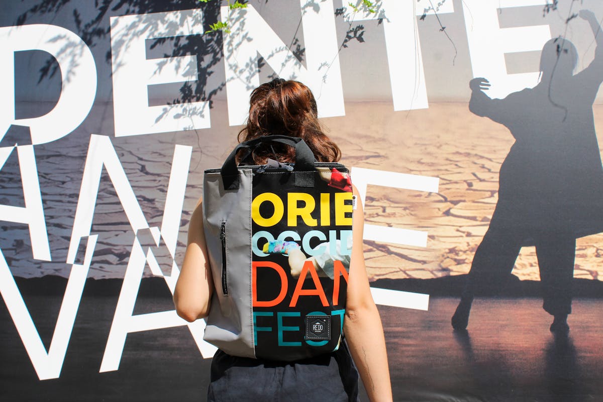 A girl from behind wearing one of our merchandising backpacks, in the background the poster of the 44th edition of the festival