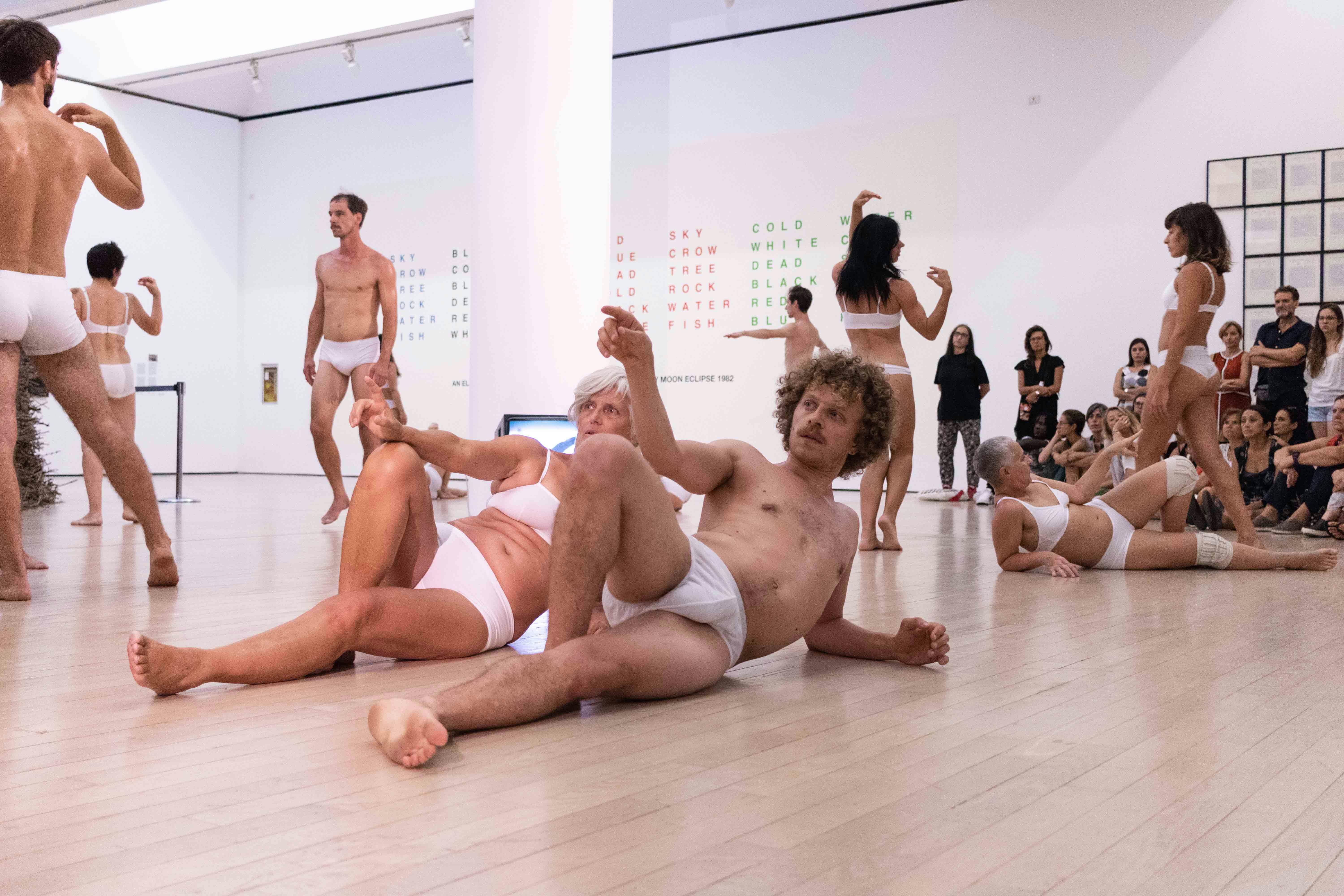 A series of performers wear only white underwear. They vary in age and dance inside a museum hall