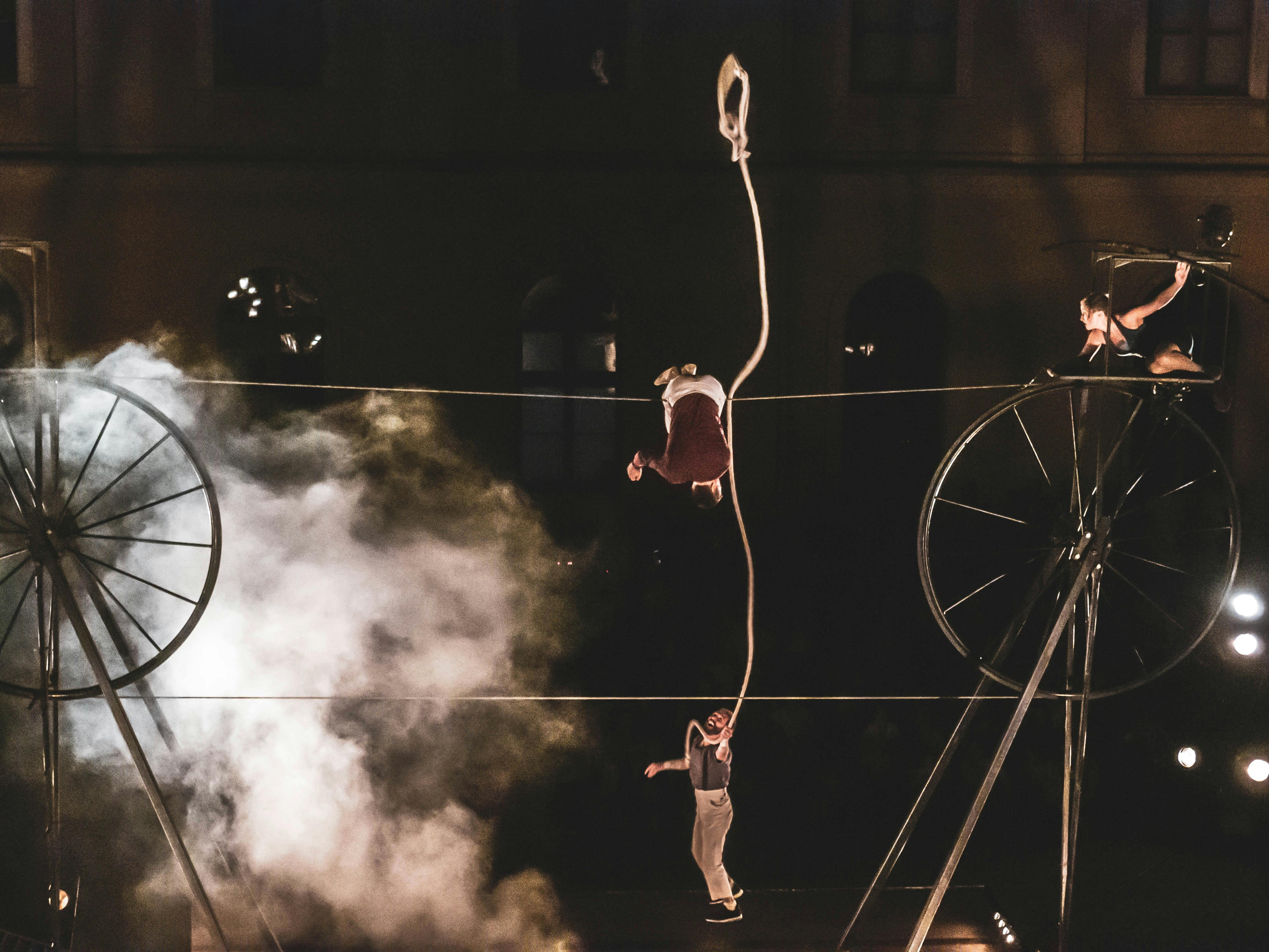 Circus performers choreograph on a structure with two large wheels joined by ropes