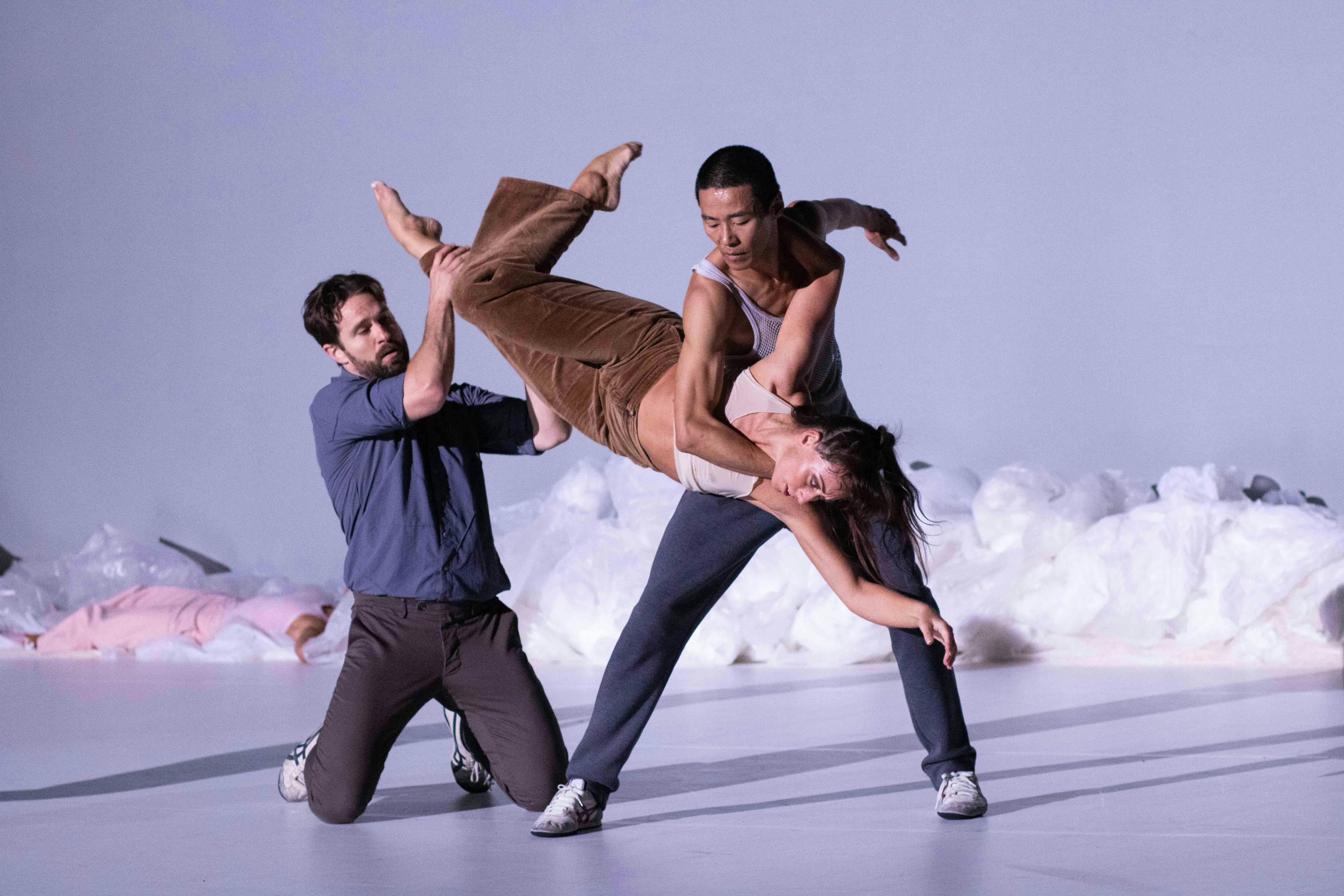 Tre performer sul palco: uno in ginocchio ed uno in piedi sorreggono una terza a testa in giù. Dietro di loro un scenografia che ricorda la neve