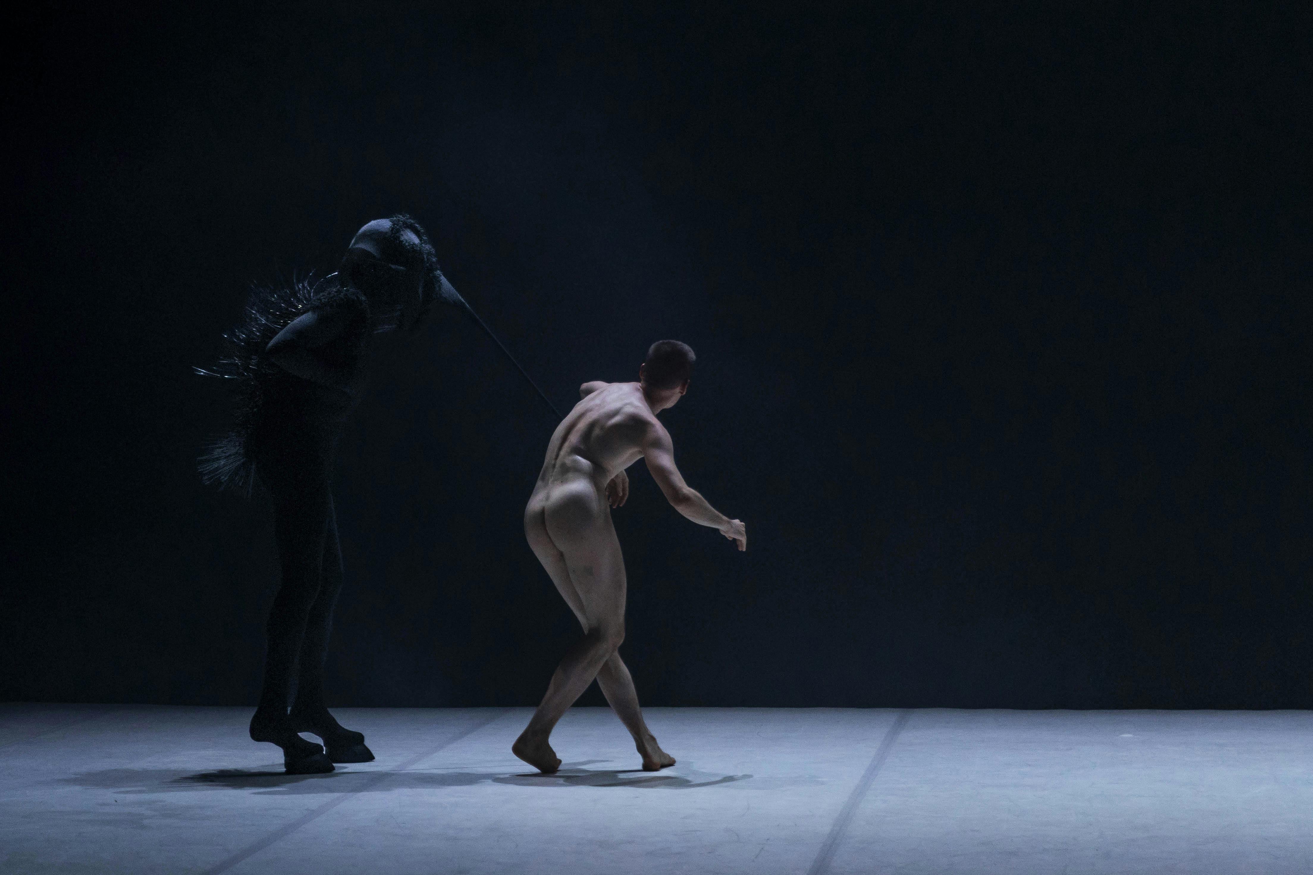 Il danzatore Nicola Galli di schiena nudo con una figura vestita di nero con  sembianze animali