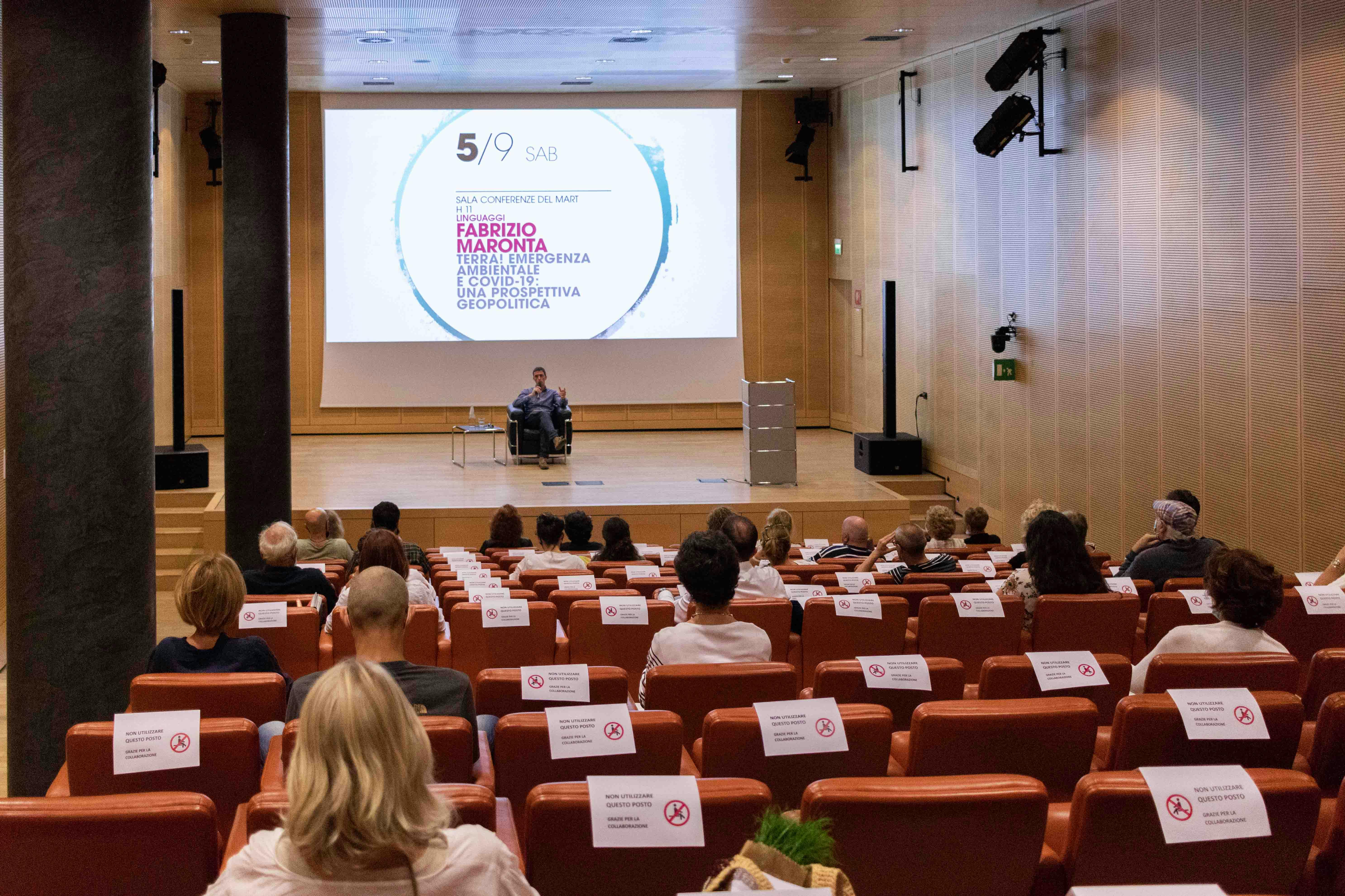 Fabrizio Maronta sul palco durante una conferenza. In primo piano la platea con il pubblico, sullo sfondo il palco.