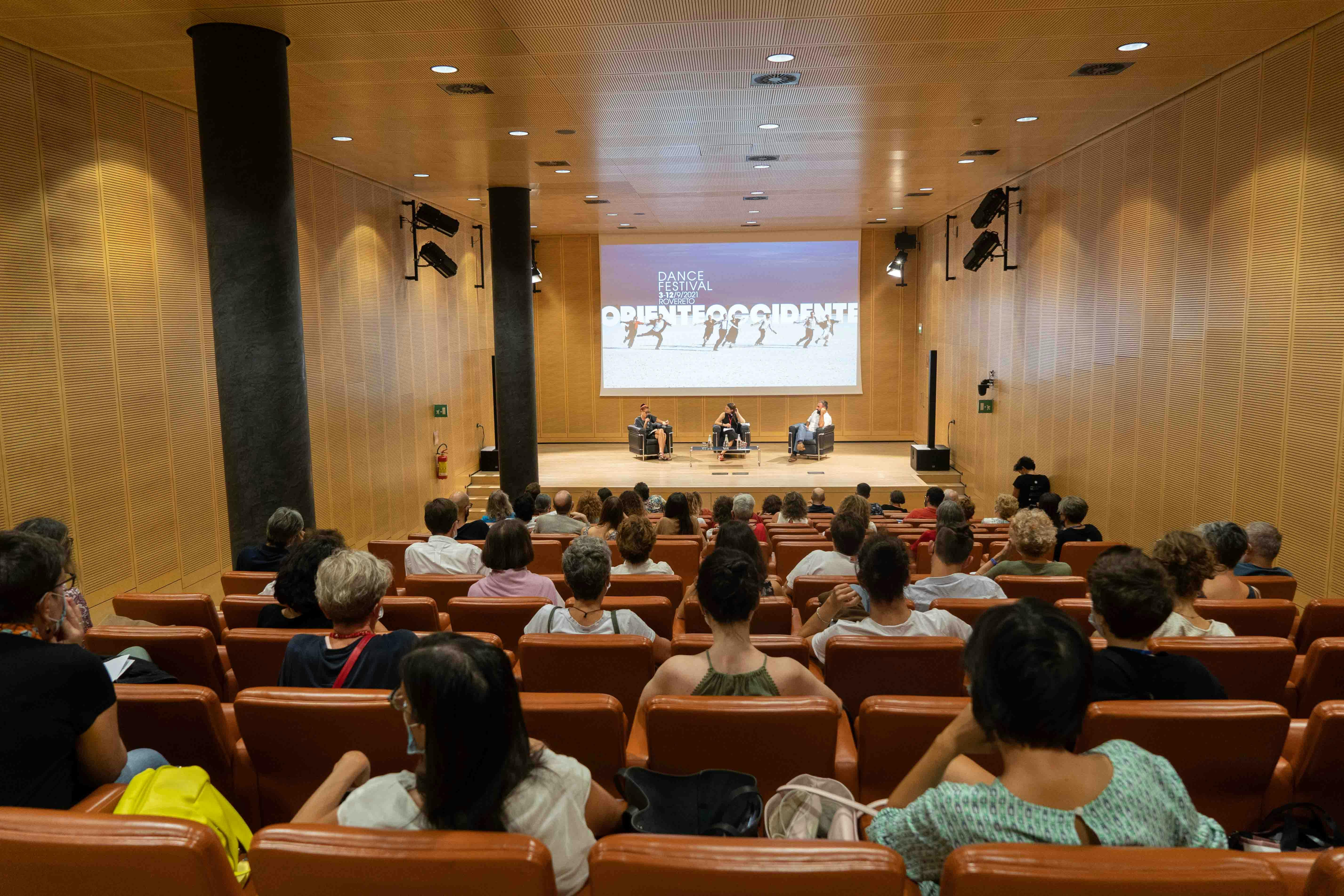 Foto della platea con il pubblico di spalle. Sullo sfondo Vera Gheno, Marco Guerini e Caterina Ghobert sul palco.