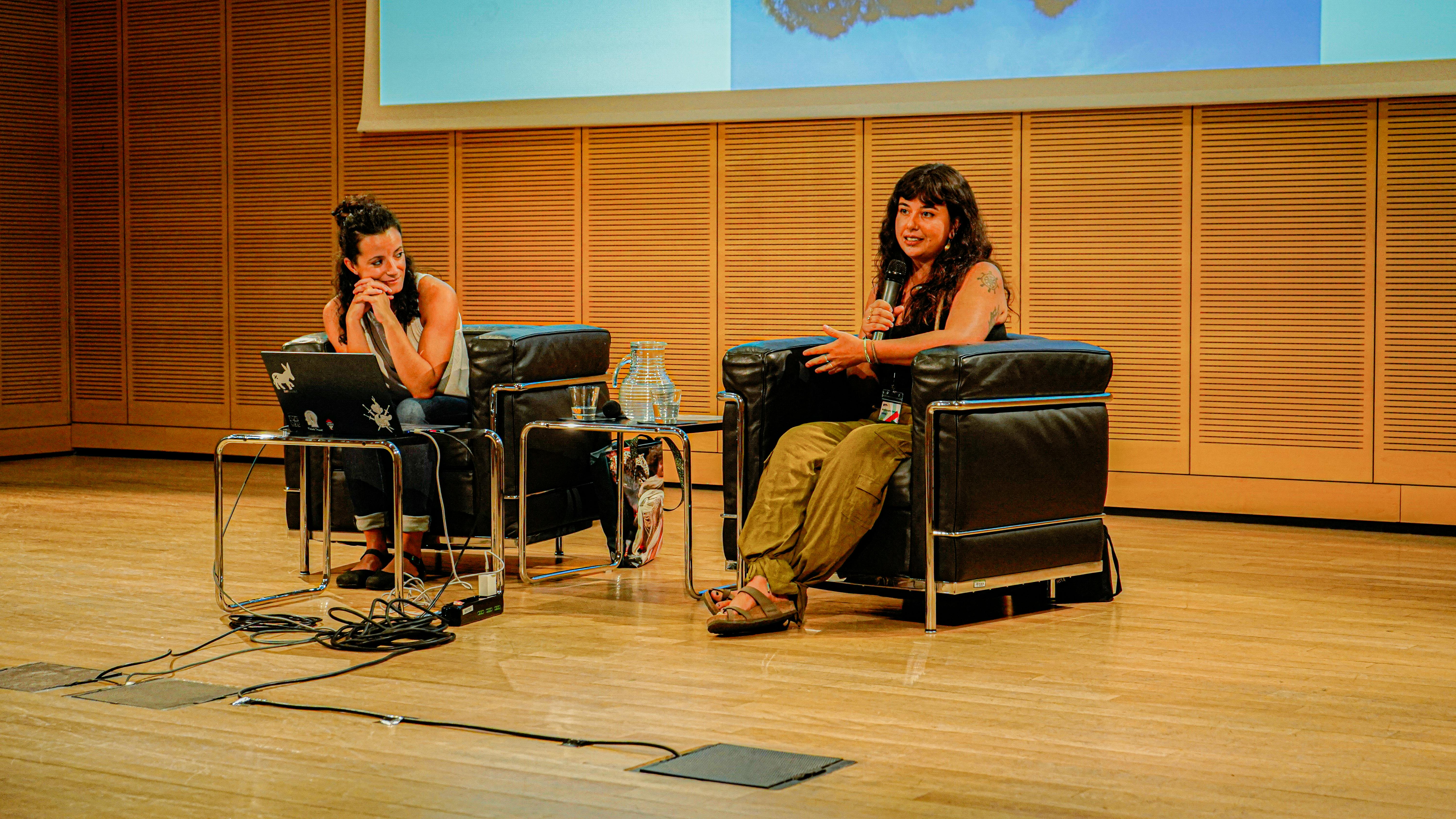 Foto di Maria Angela Clemente e Francesca Simi sul palco, durante una conferenza. Una delle due sta parlando al microfono.