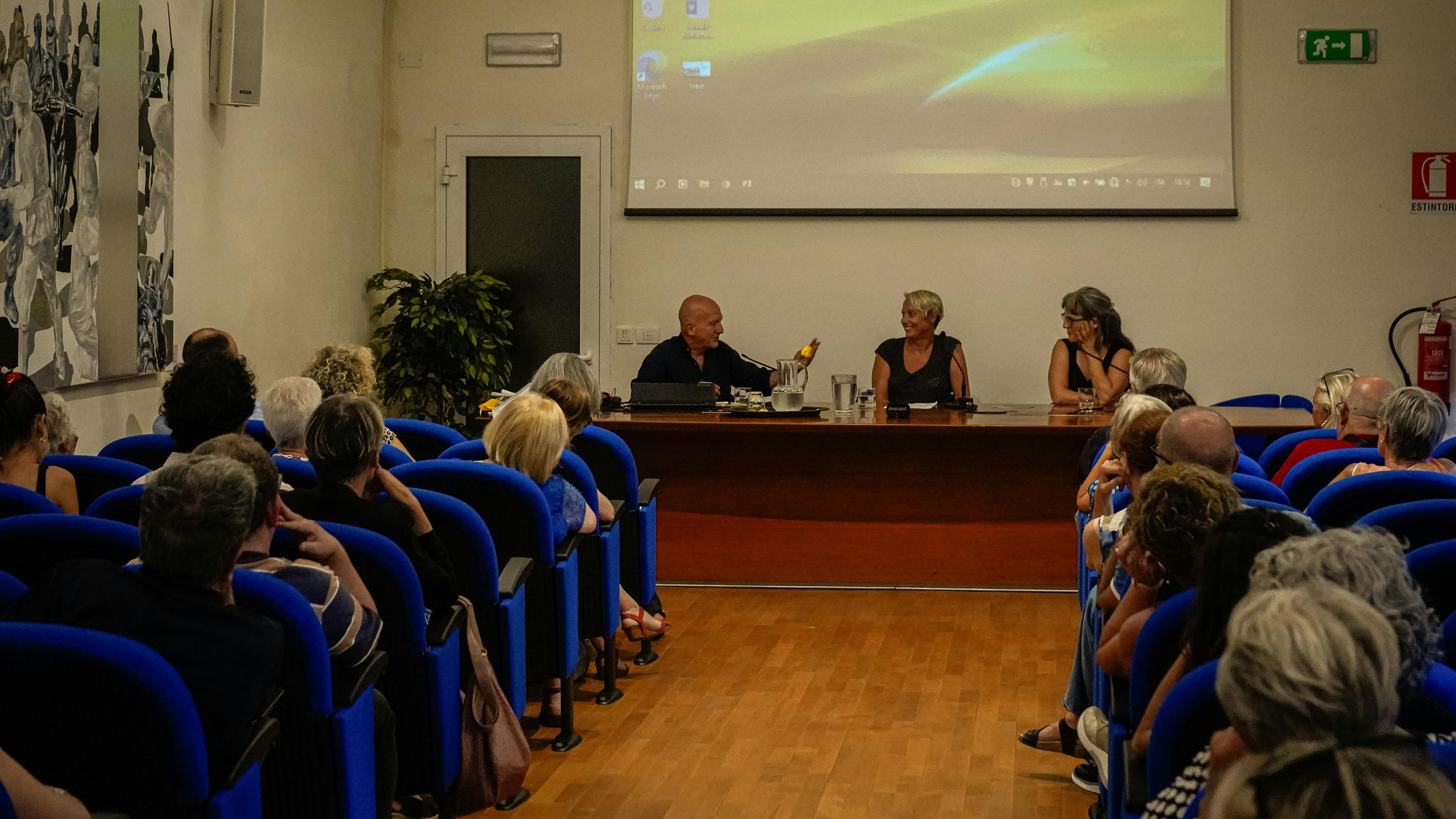 In primo piano una platea con il pubblico di spalle. Ascoltano Mario Boccia, Anja Margetić e Benjamina Karić