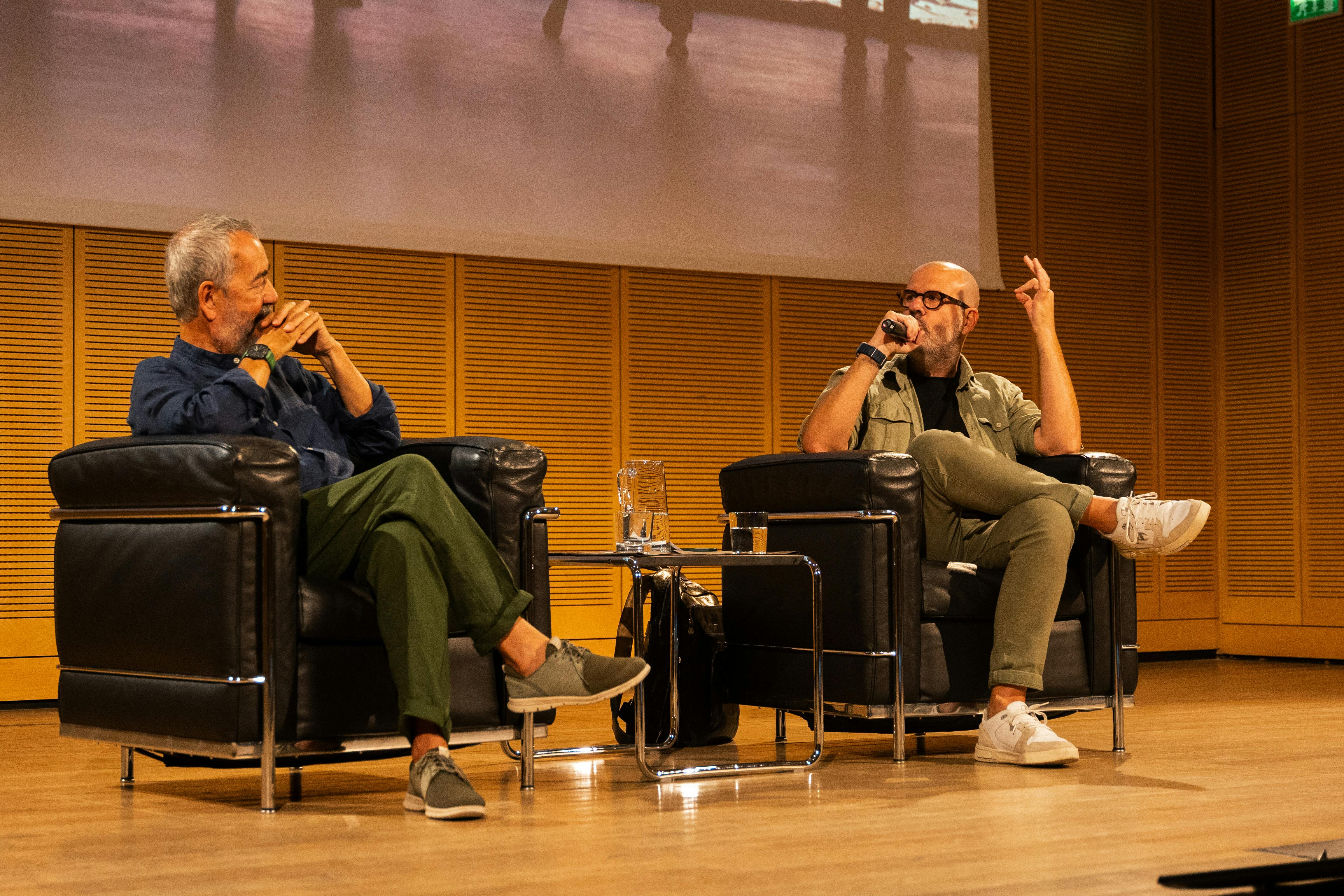 Foto di Raffaele Crocco e Nello Scavo durante una conferenza. Sono entrambi seduti su delle poltrone nere. Nello Scavo sta parlando al microfono.