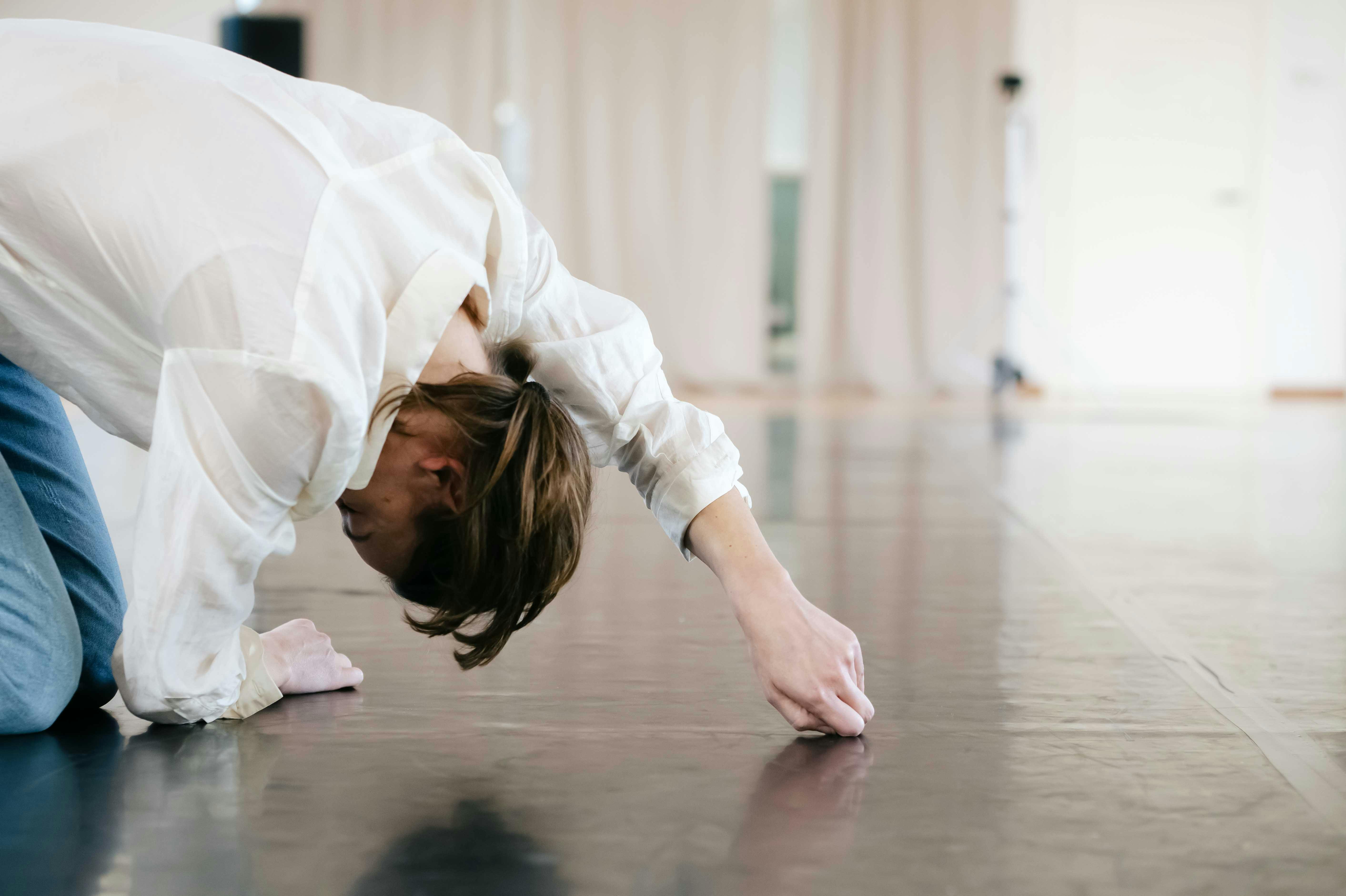 Stefania Tansini is wearing a white shirt, is kneeling with her torso forward, is resting on the ground with her right forearm and left arm extended forward