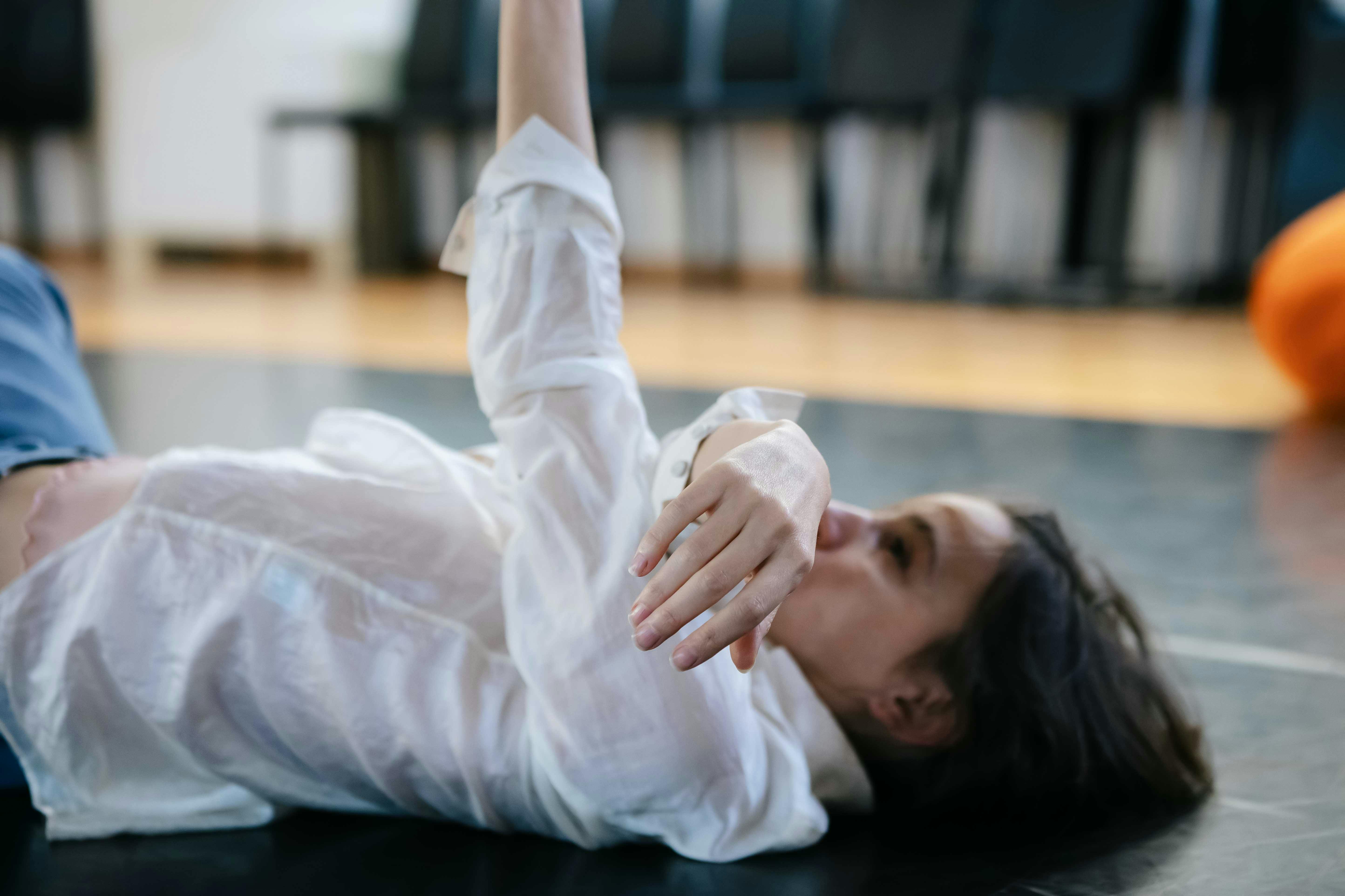 Stefania Tansini is wearing a white shirt, she is lying on the floor with one arm stretched towards the ceiling and the other covering the lower part of her face