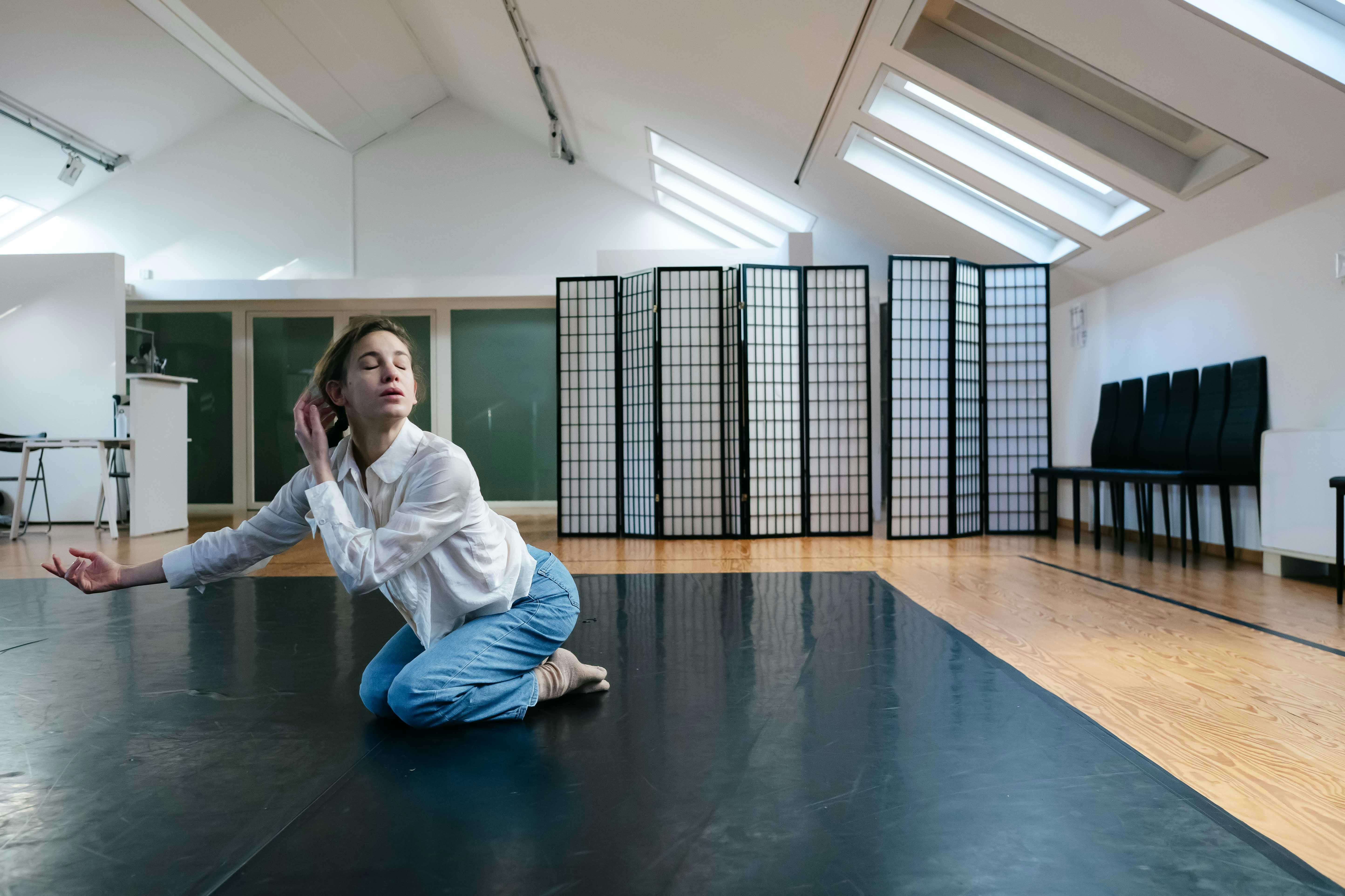 Stefania Tansini on her knees with her torso stretched forward, one arm in suspension extended to the left and the other close to her ear