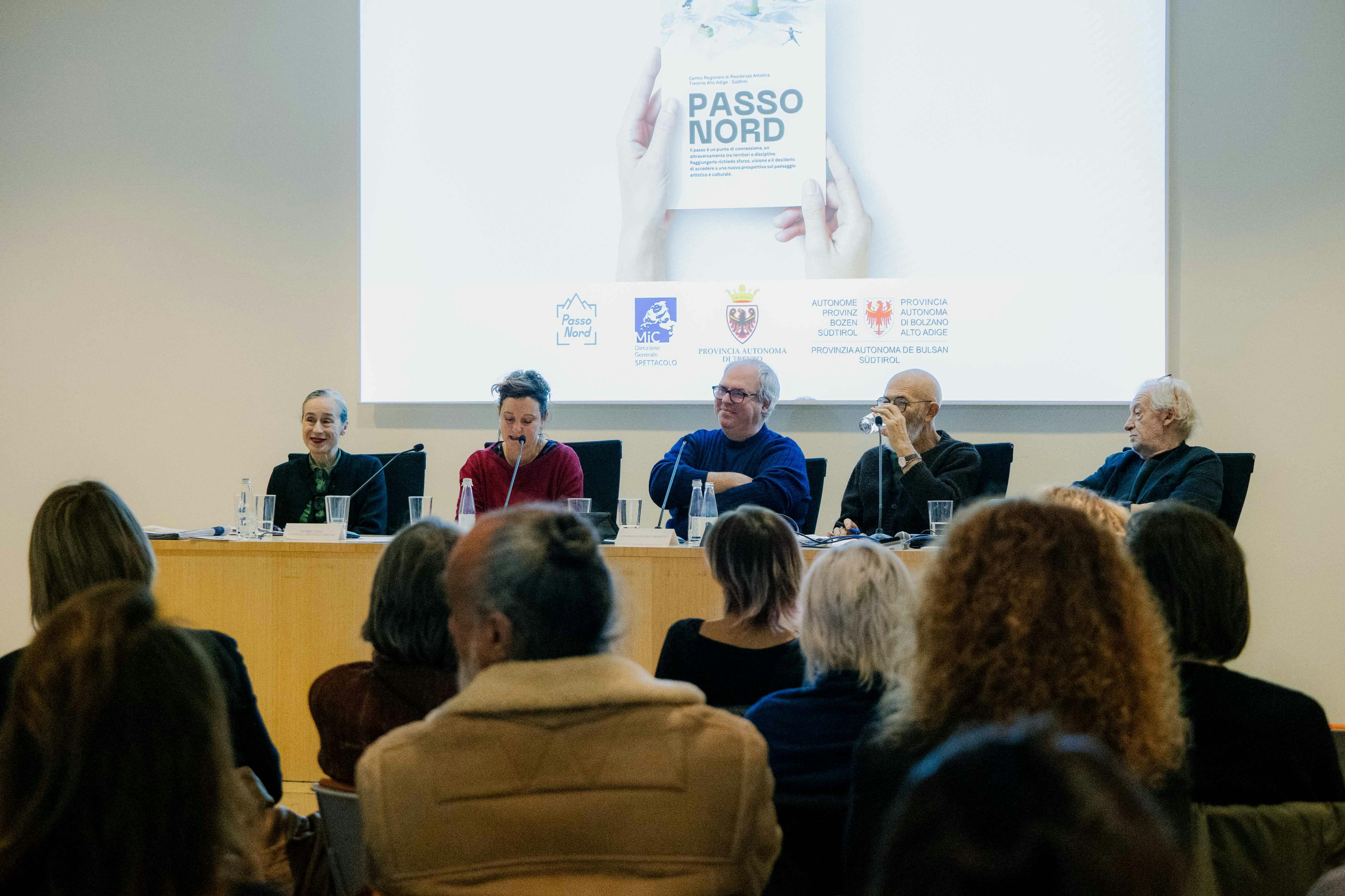 Cinque persone sedute a un tavolo di una sala conferenze, di schiena il pubblico seduto ad ascoltare.