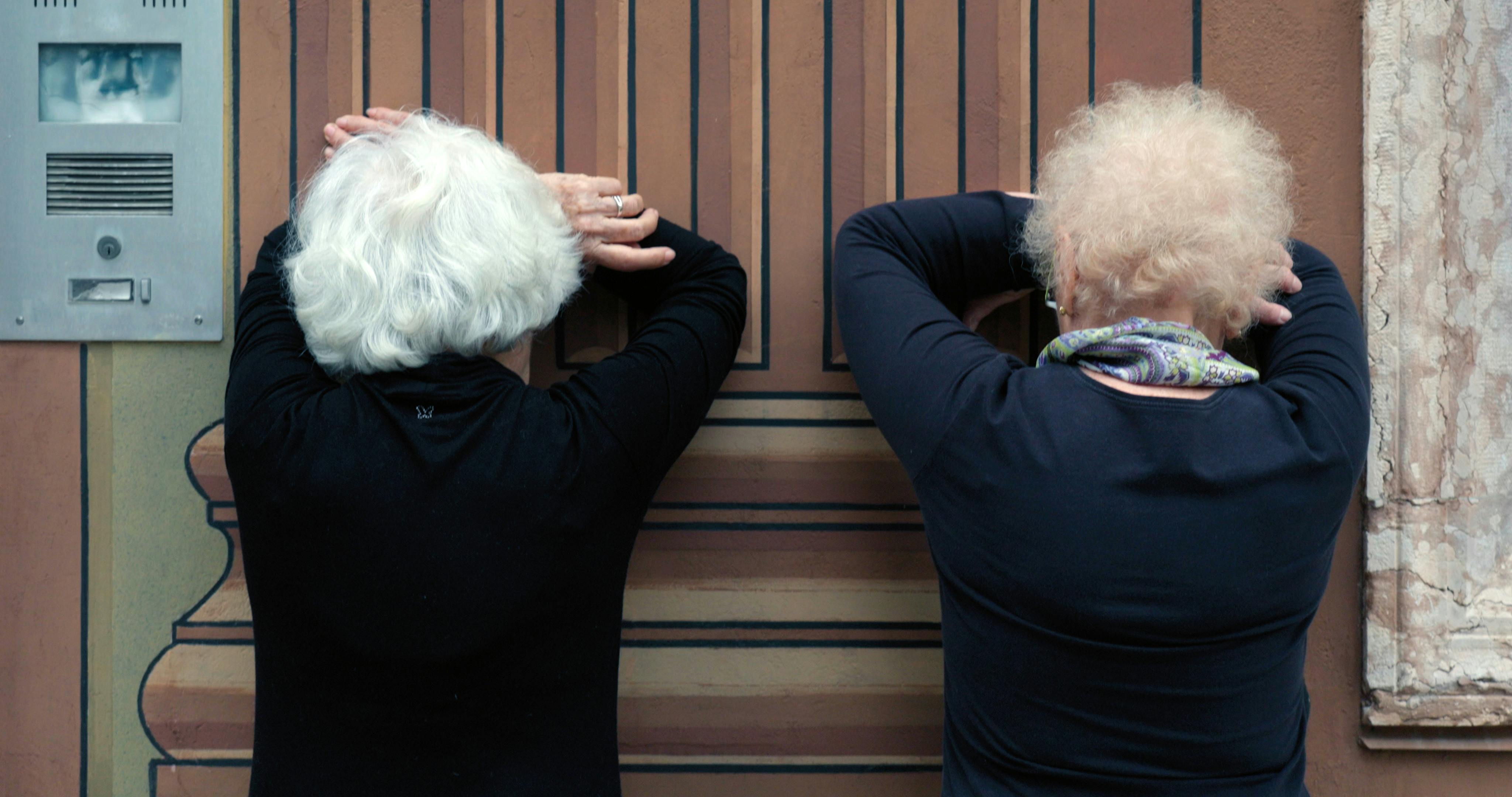 Due signore di spalle, con il viso rivolto al muro e appoggiato alle braccia