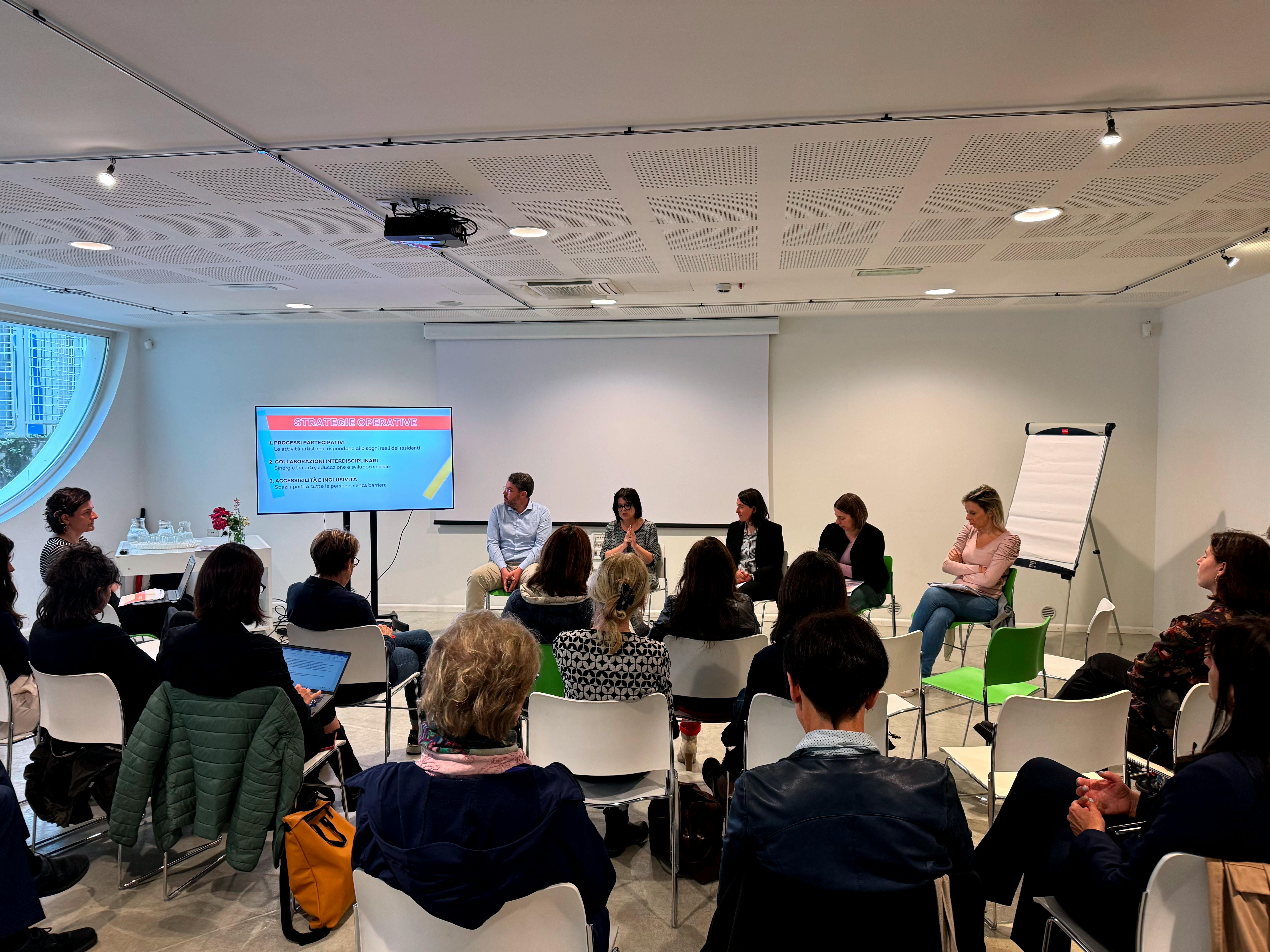 Sala dell'Urban Center con persone sedute che ascoltano gli interventi della conferenza stampa