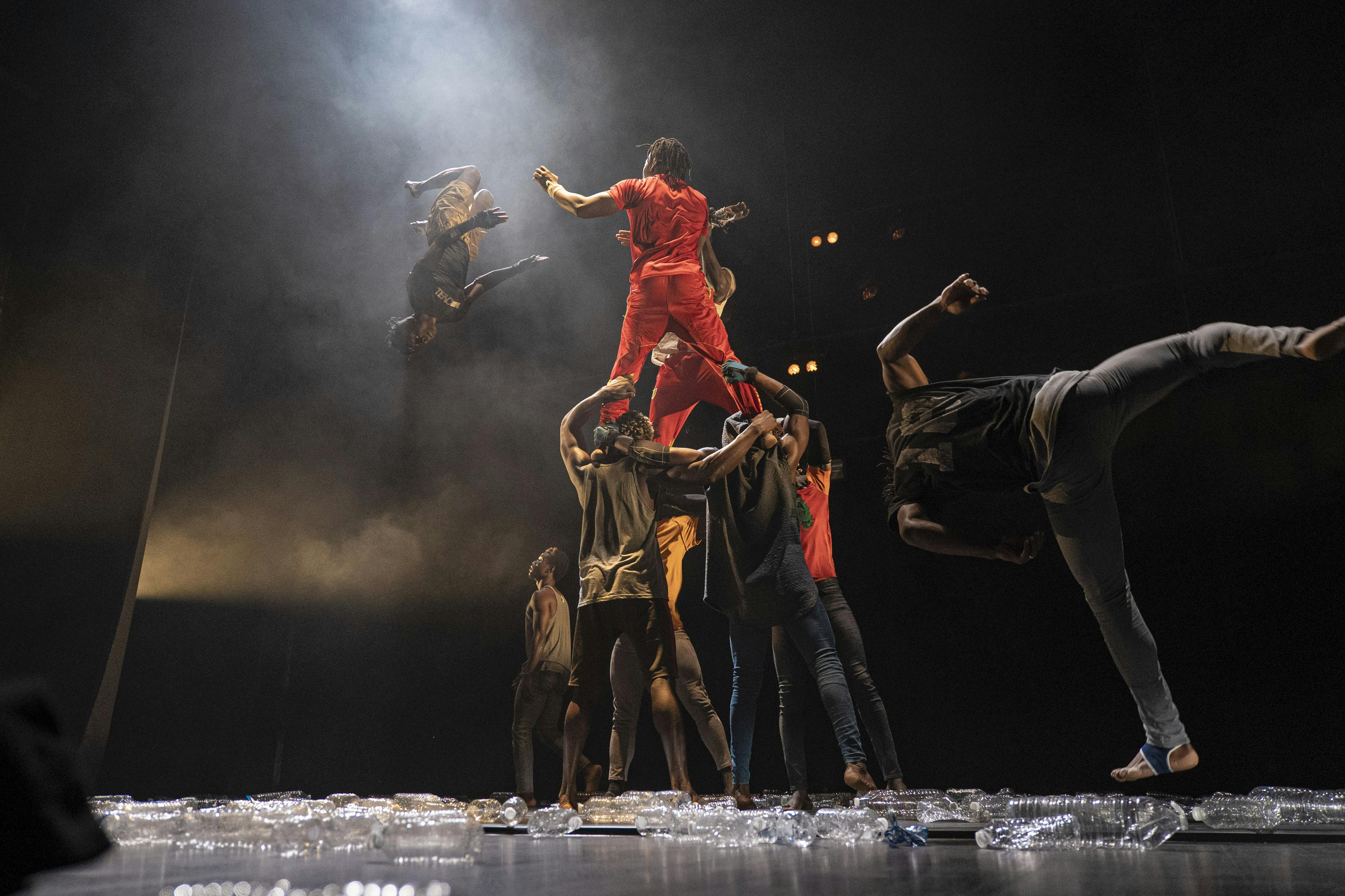Un gruppo di danzatori con abiti scuri si esibisce in movimenti acrobatici sul palco