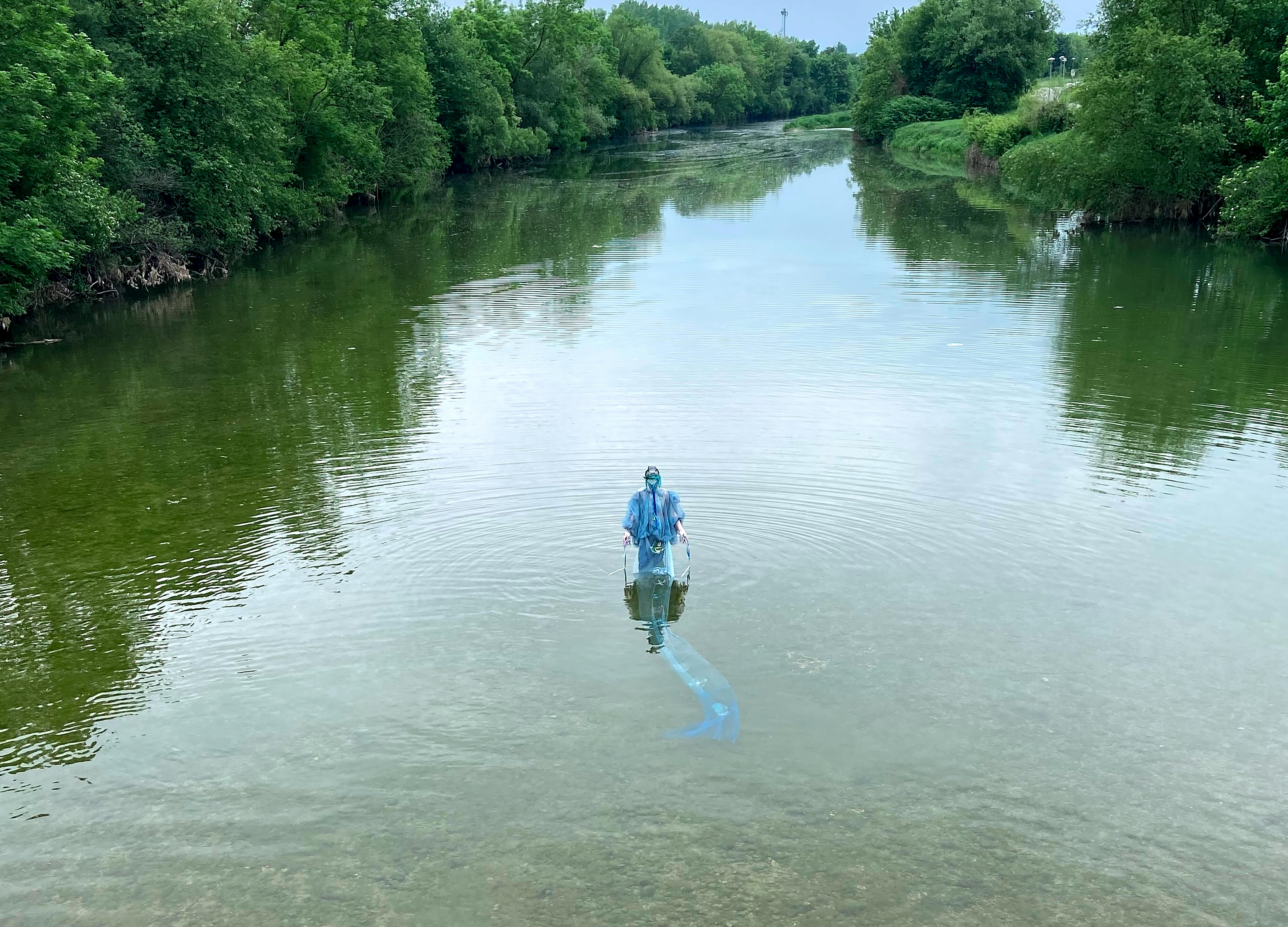 Una persona vestita con una tuta azzurra in piedi in mezzo a un fiume l'acqua arriva alle ginocchia