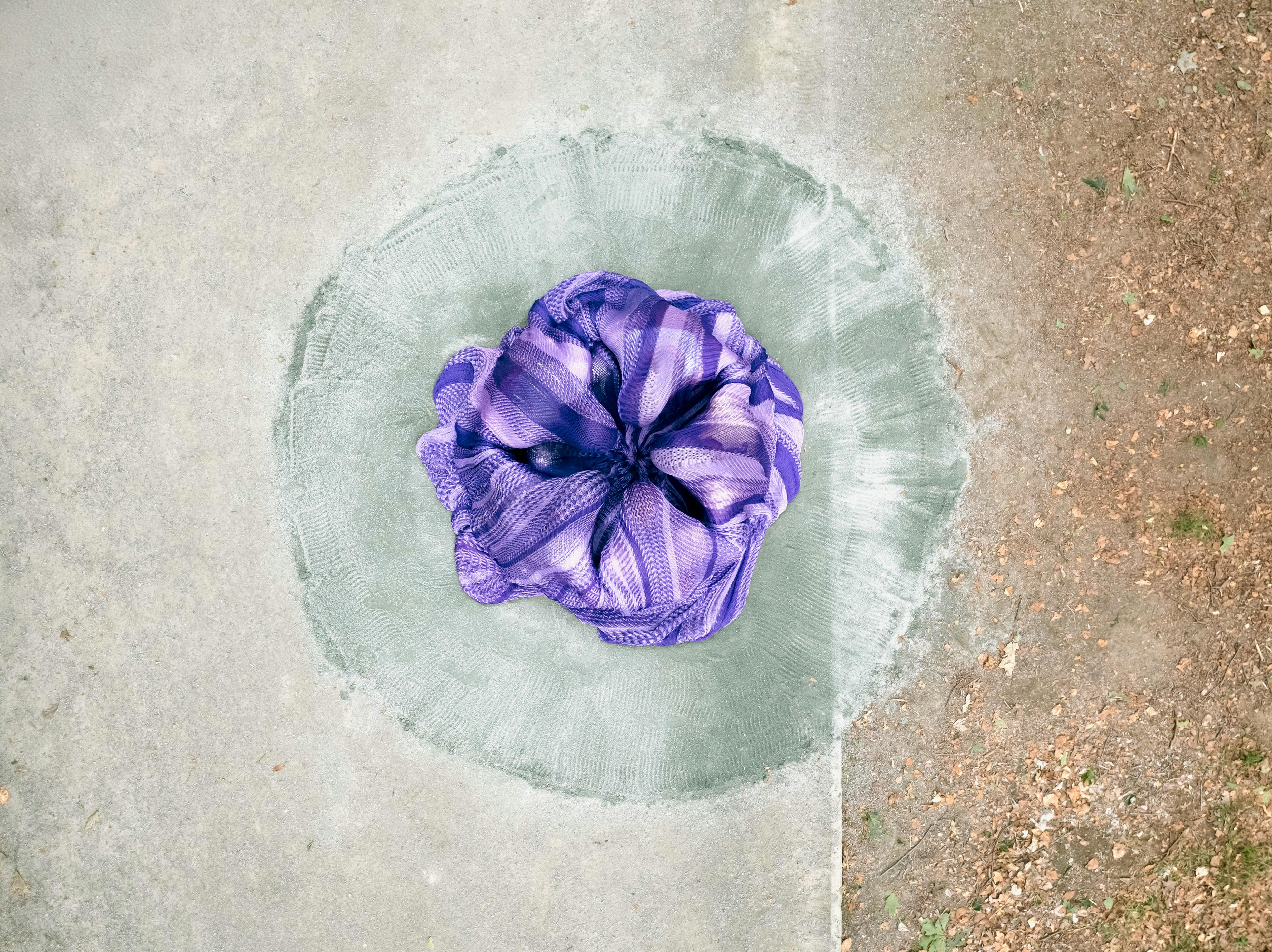 A set of purple fabrics creates a circular shape that resembles a flower. This shape is inside a circle drawn on the ground. The whole is seen from above