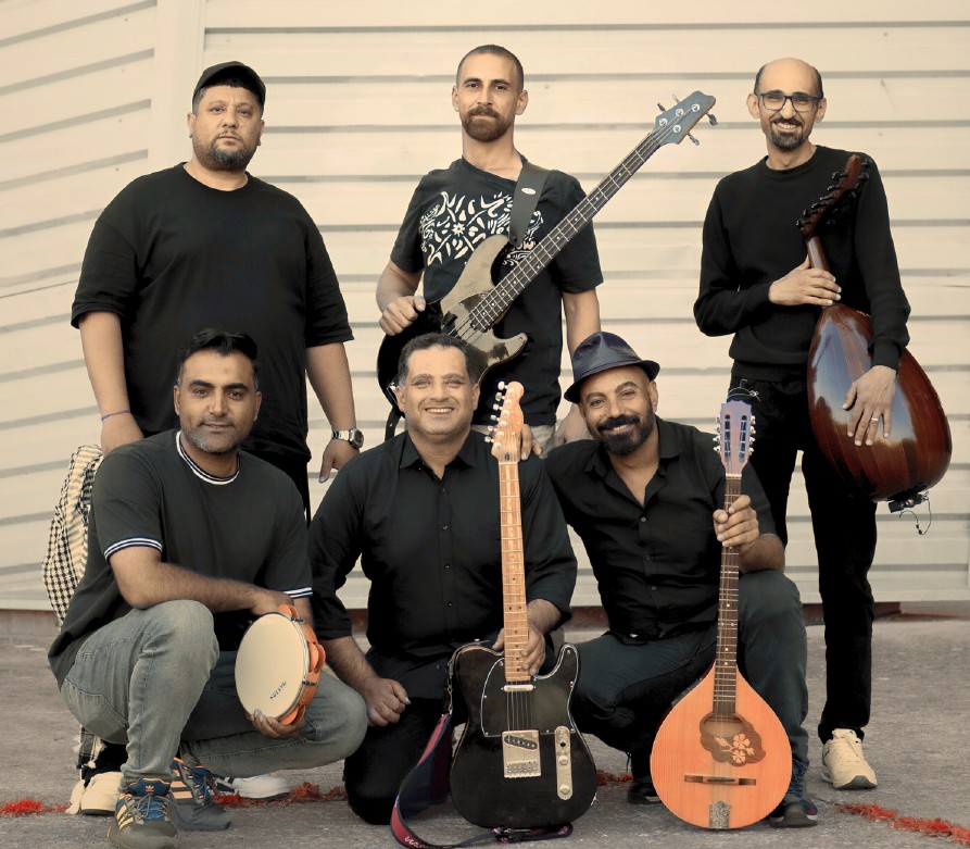Sei uomini, tre in piedi, tre inginocchiati sorridono con in mano i loro strumenti musicali: percussioni, chitarre, strumenti tradizionali del Medio Oriente
