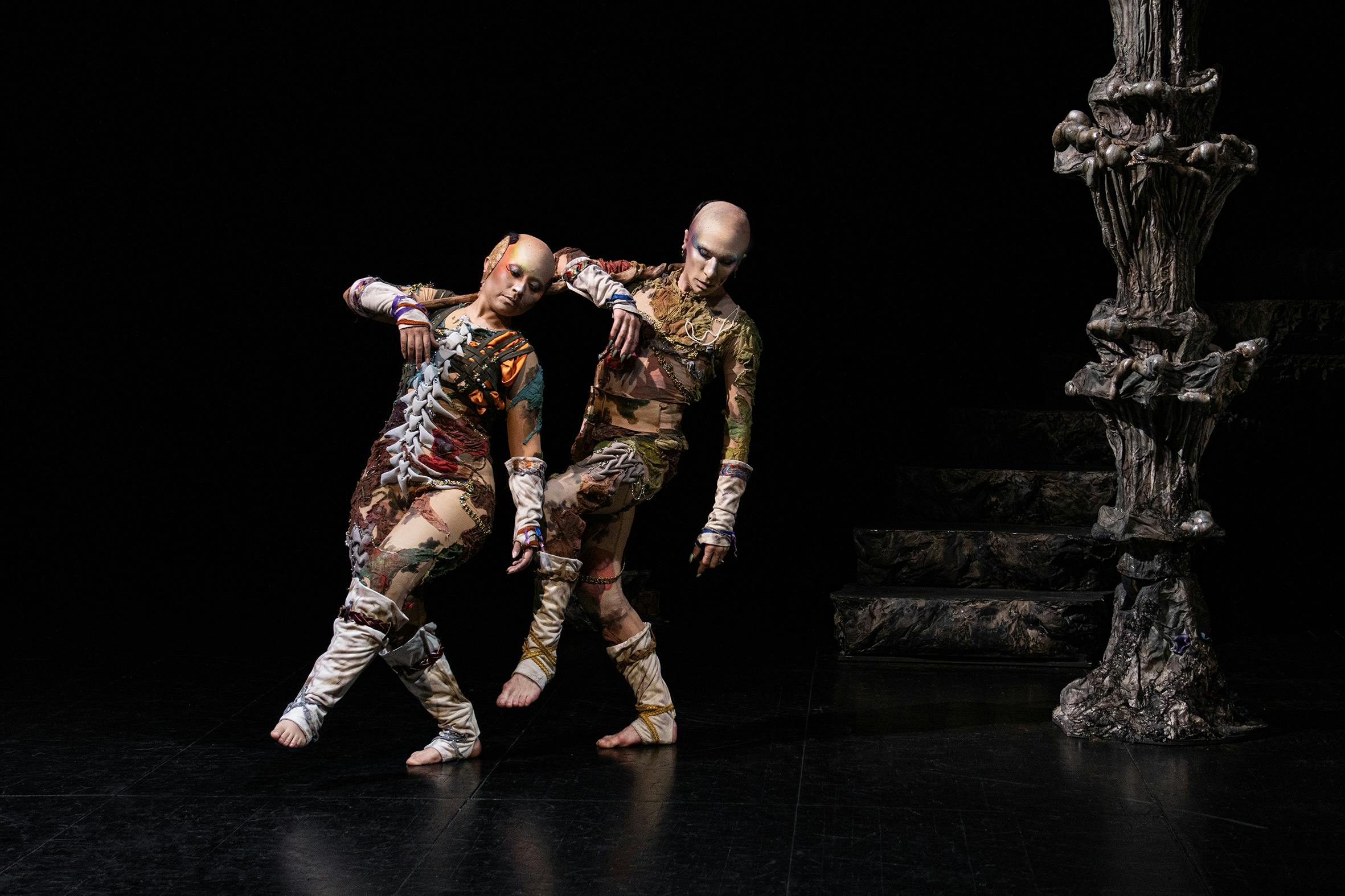 The two performers on stage wear colourful outfits reminiscent of a fantasy world