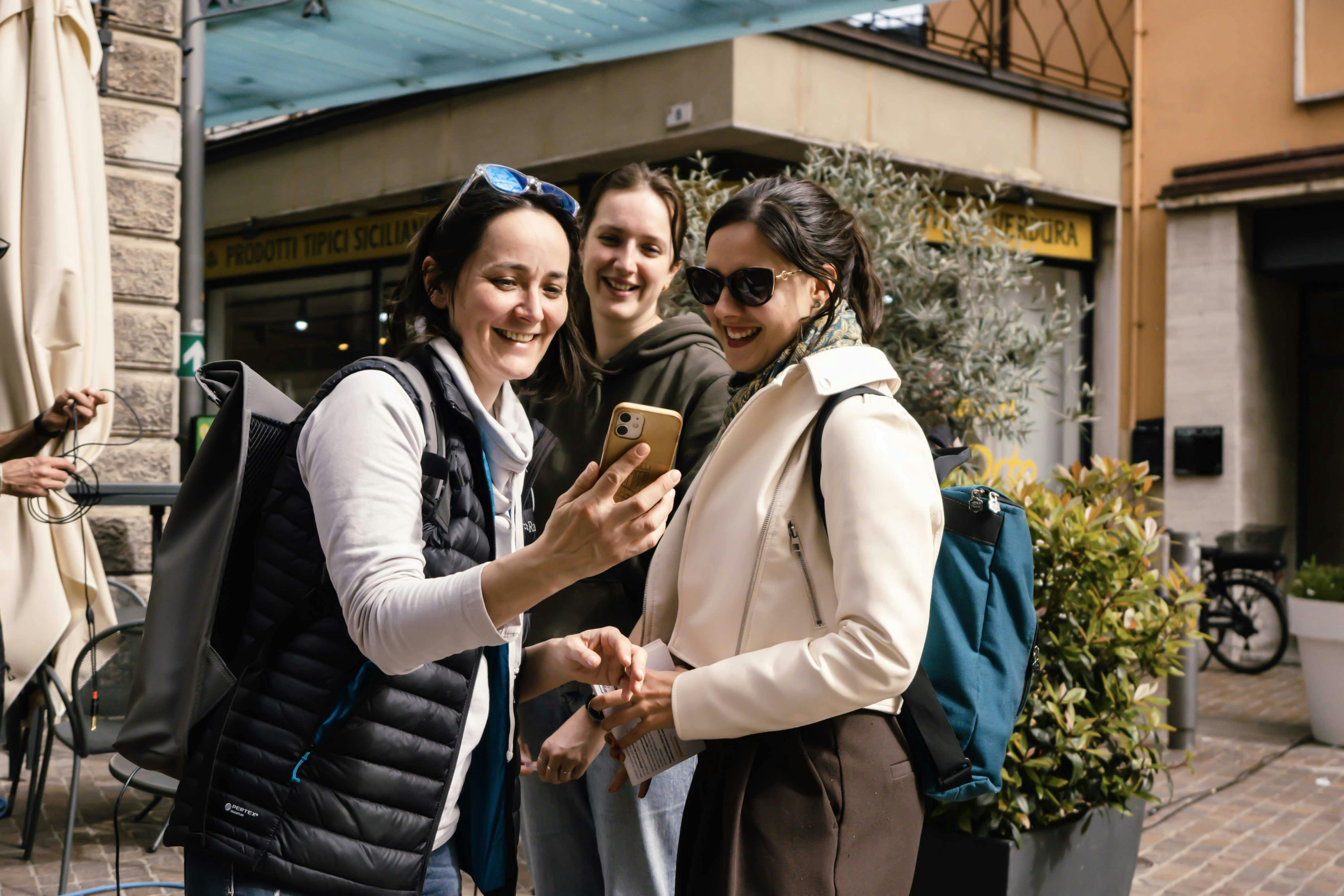 Laura, Lucrezia e Rebecca guardano lo schermo di un telefono sorridendo