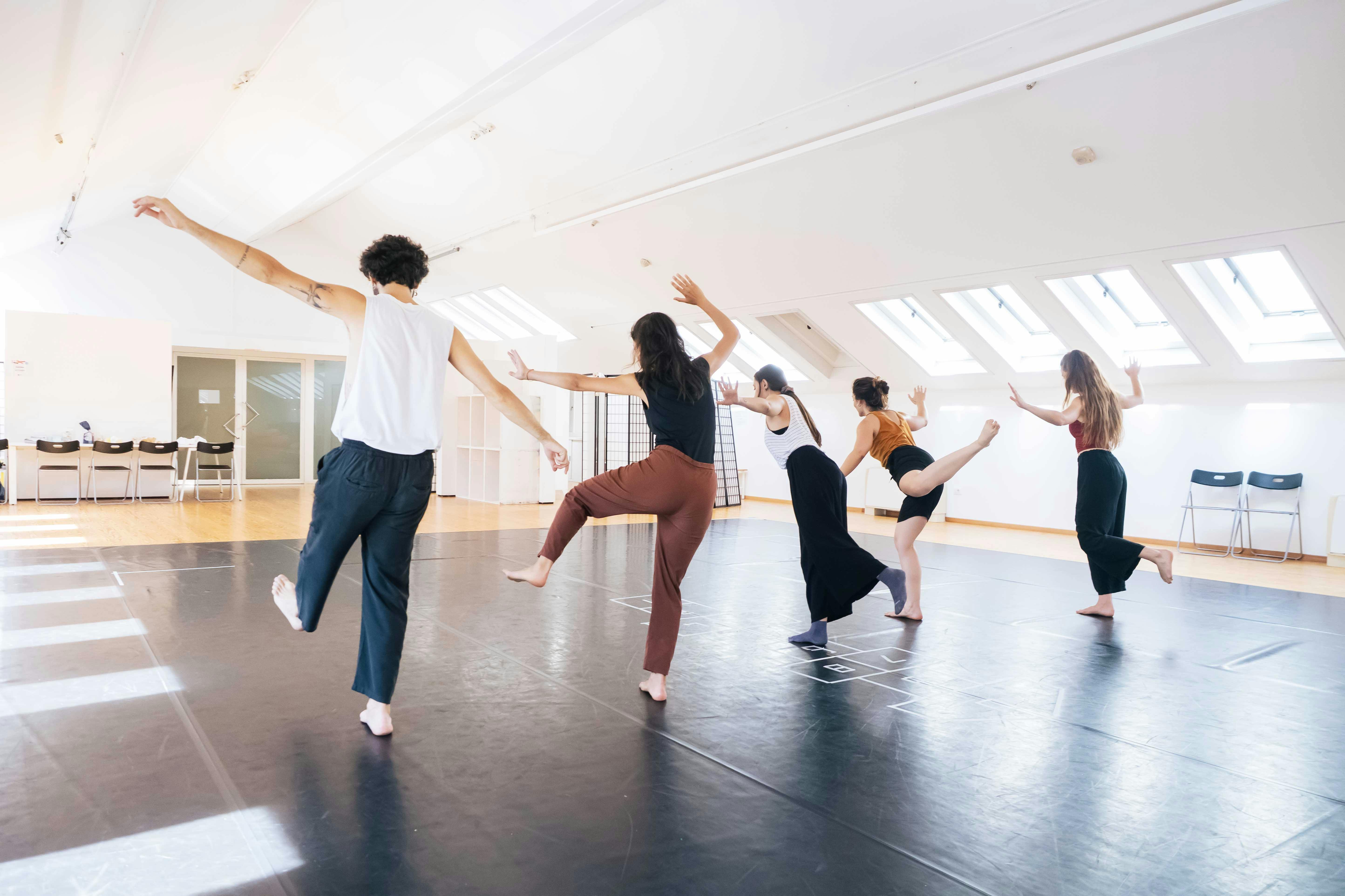 Cinque performer in sala danza giocano a stare in equilibrio su una sola gamba