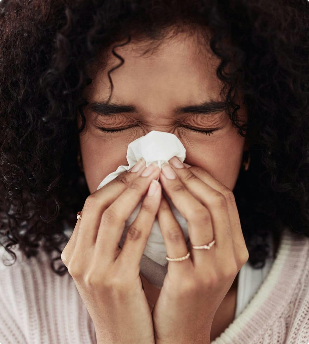 a woman with dark hair blowing her nose with a tissue