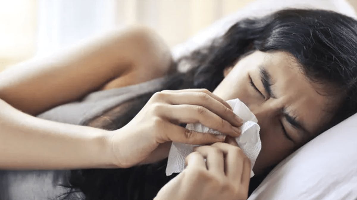 Woman blowing her nose in bed.