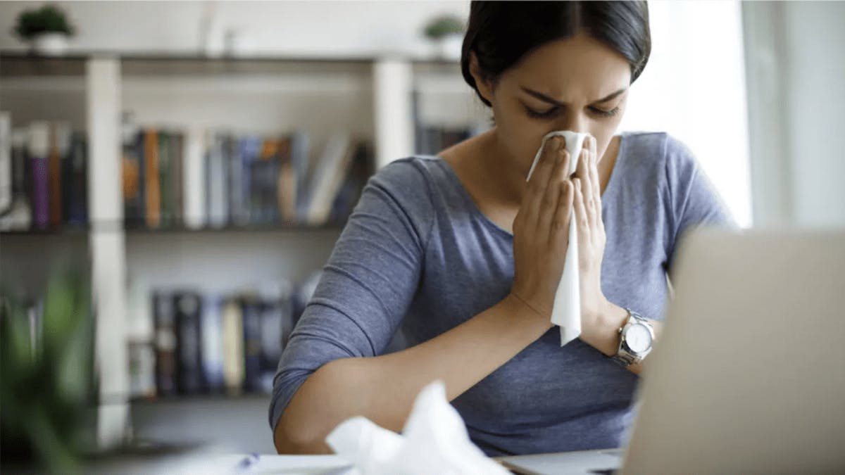 an image of a woman in a grey top blowing her nose