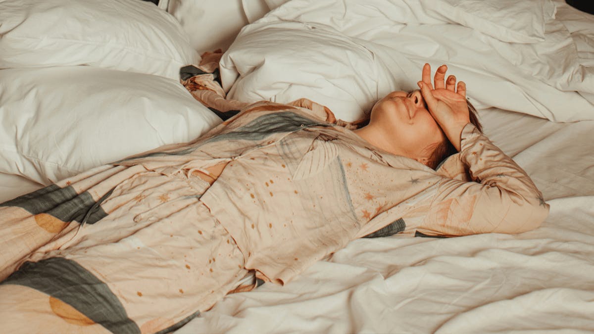 an image of female laying in a bed with her hand up to her head