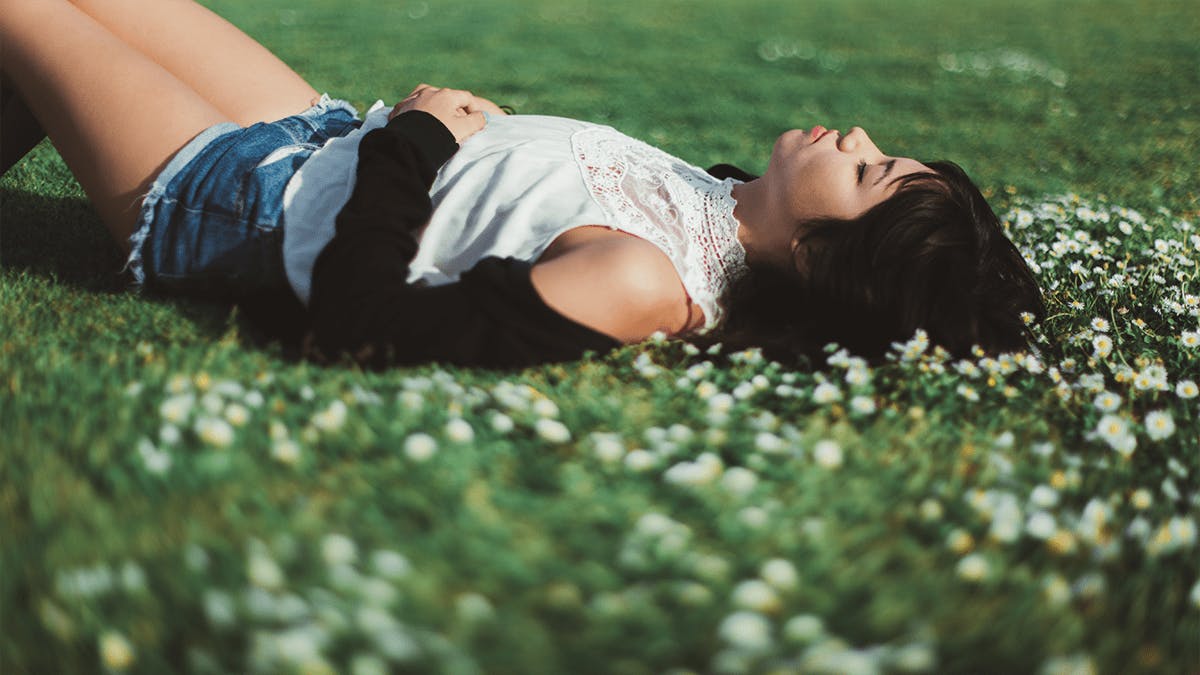 Woman lying on grassy ground with flowers. 