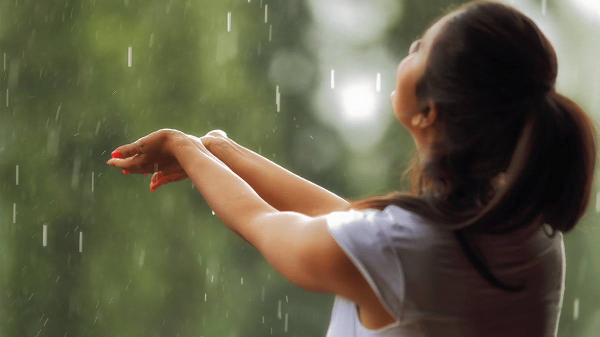 an image of a woman holding her hands out into the rain