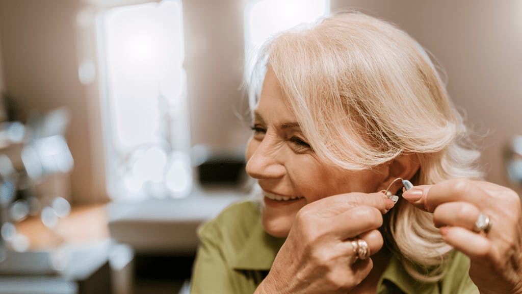 Older woman putting on a hearing aid.
