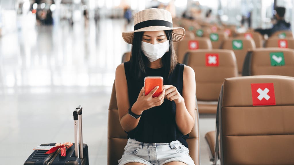 an image of a woman at the airport on her phone wearing a mask