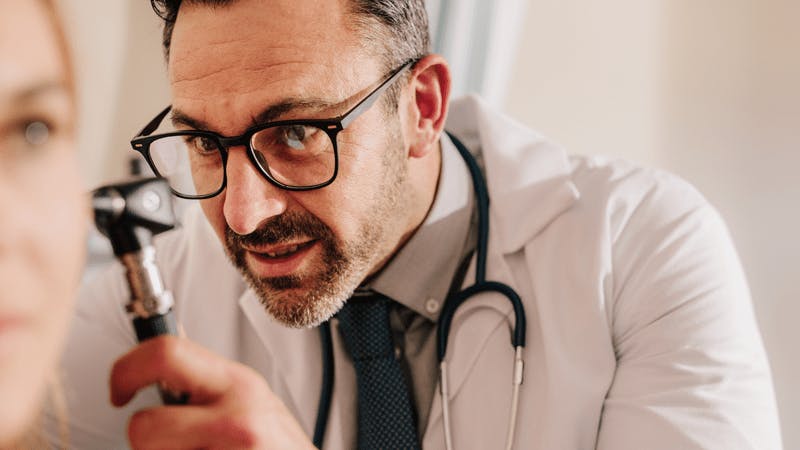 a male doctor doing a ear exam on a woman