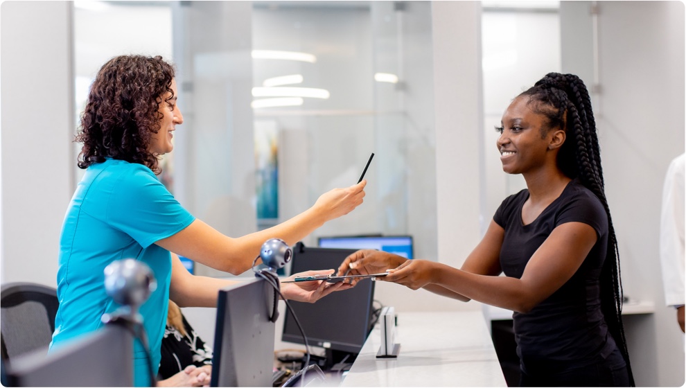 a patient handing a front desk staff memeber her paperwork