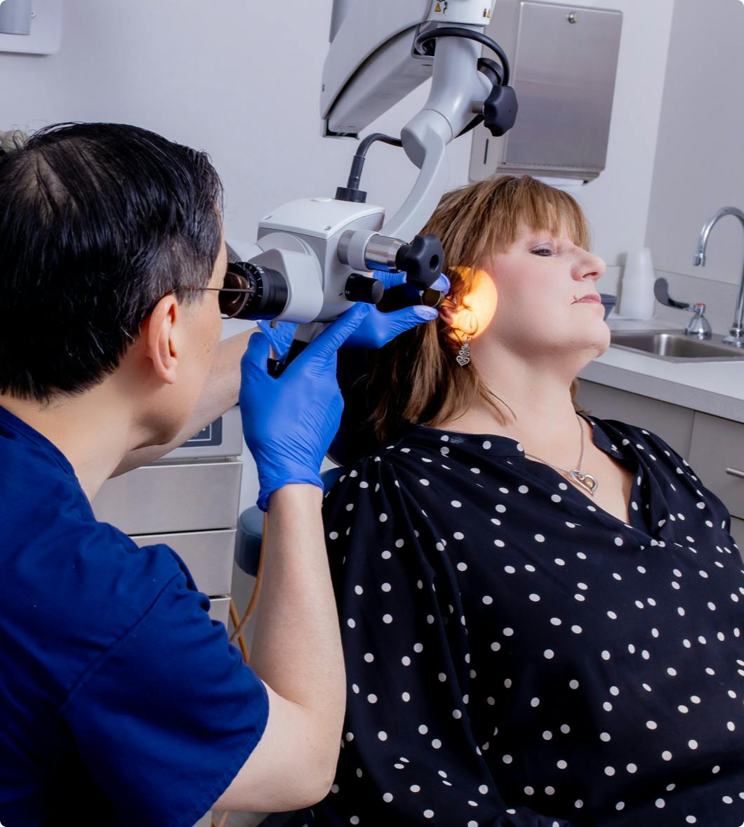 a doctor doing an ear exam on a female patient in a black top