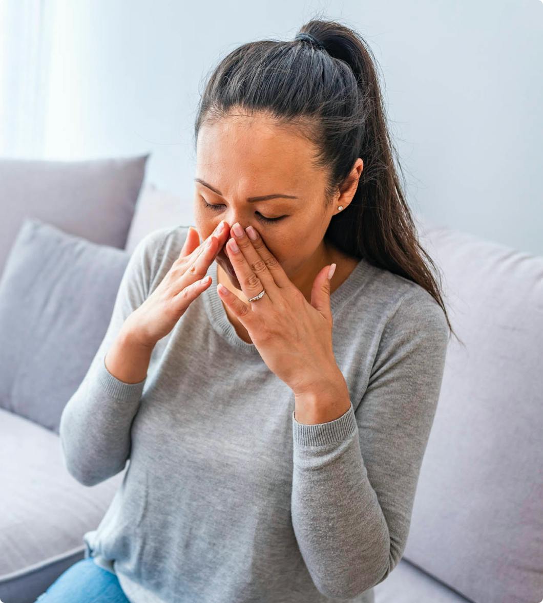 a woman in a grey long sleeve holding her hands up to her sinuses