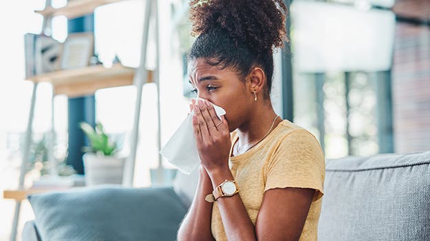 a woman sitting on a couch blowing their nose into a tissue