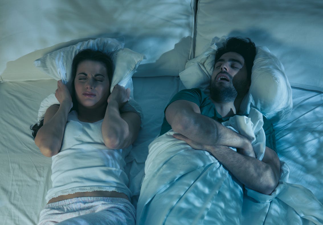 Woman in bed frustrated and trying to sleep next to man sleeping soundly.