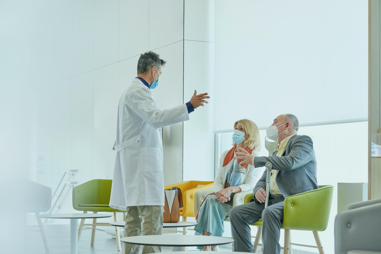 a doctor walking to two patients with mask in a hospital lobby
