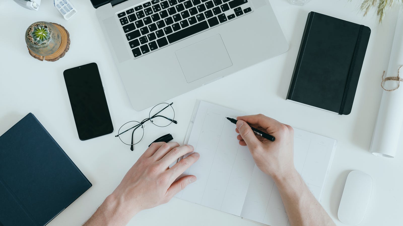 a close up of a desk with a notebook, glasses and laptop