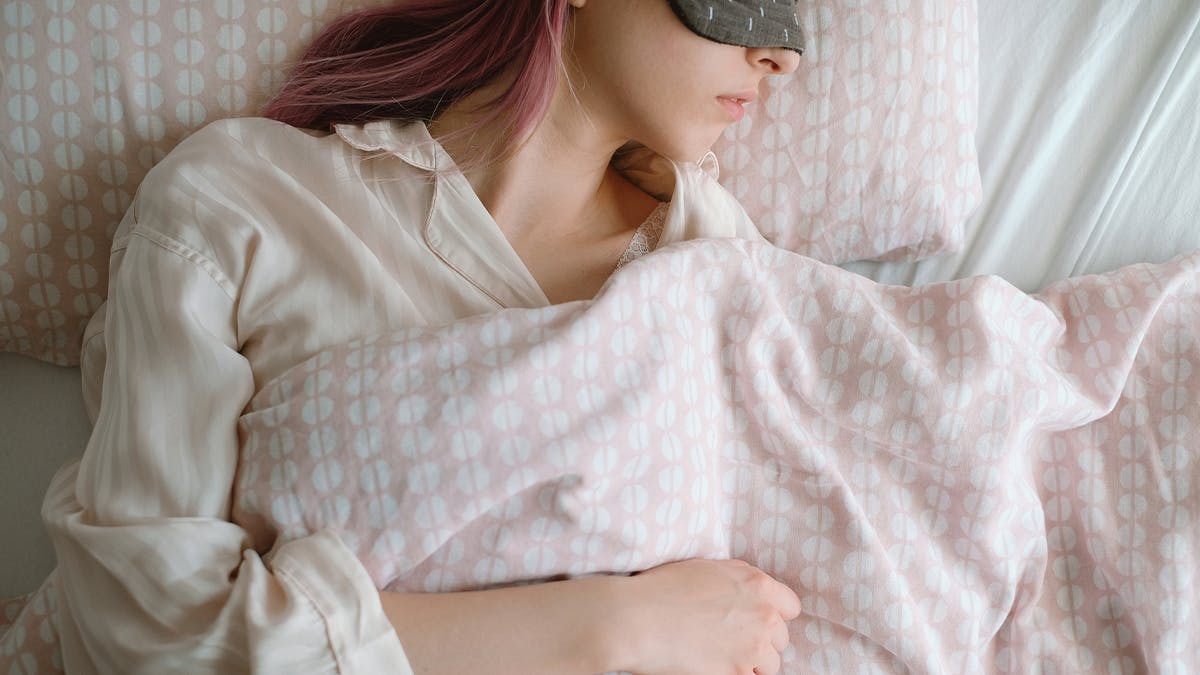 an image of a young woman sleeping in bed with an eye mask