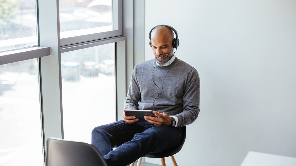 an image of a man wearing headphones looking at an ipad