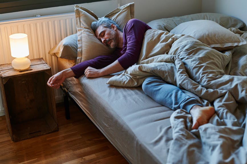 a man sleeping in his bed with a bedside lamp