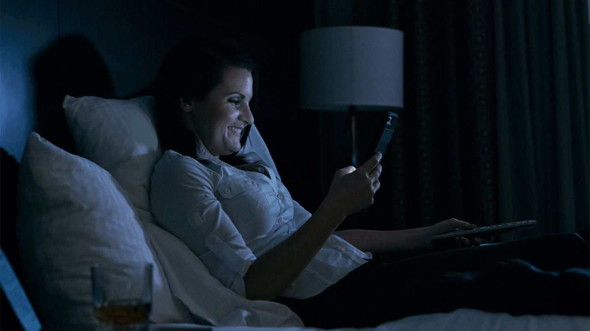 an image of a woman sitting on the bed in the dark on her phone