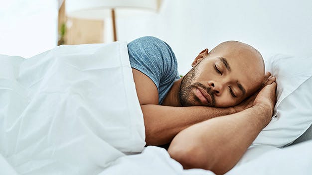 a man sleeping in a bed with white sheets