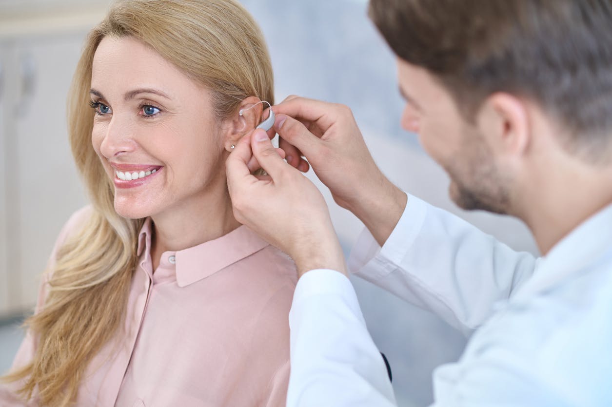 Doctor assisting woman with putting on her hearing aid