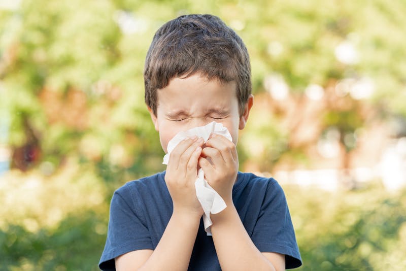 Child sneezing into a tissue outside